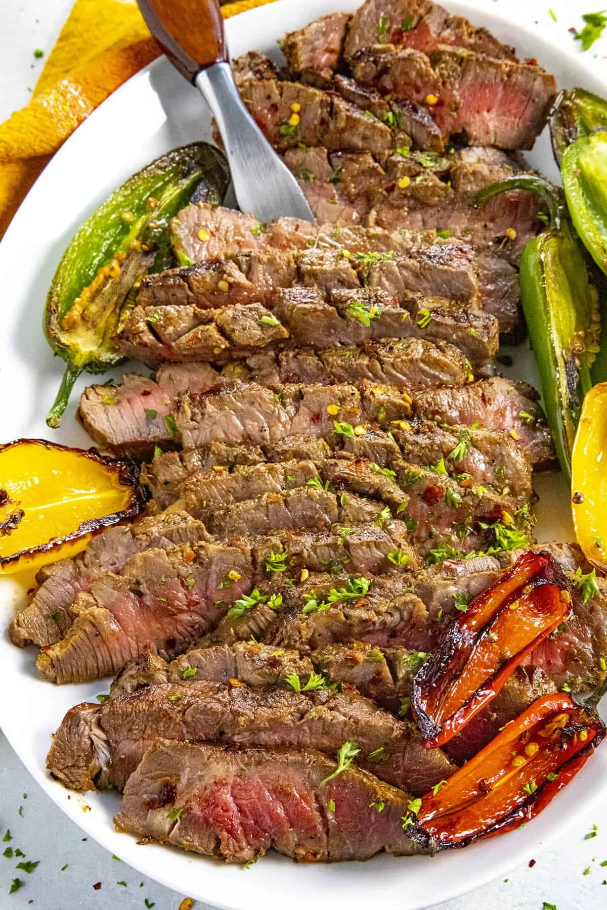 Serving sliced London broil on a platter with grilled peppers