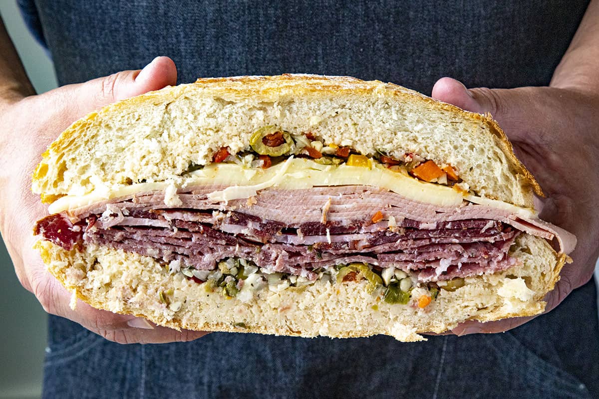 A thick and meaty Muffaletta sandwich sliced in half, showing all of the layers of meats and cheese