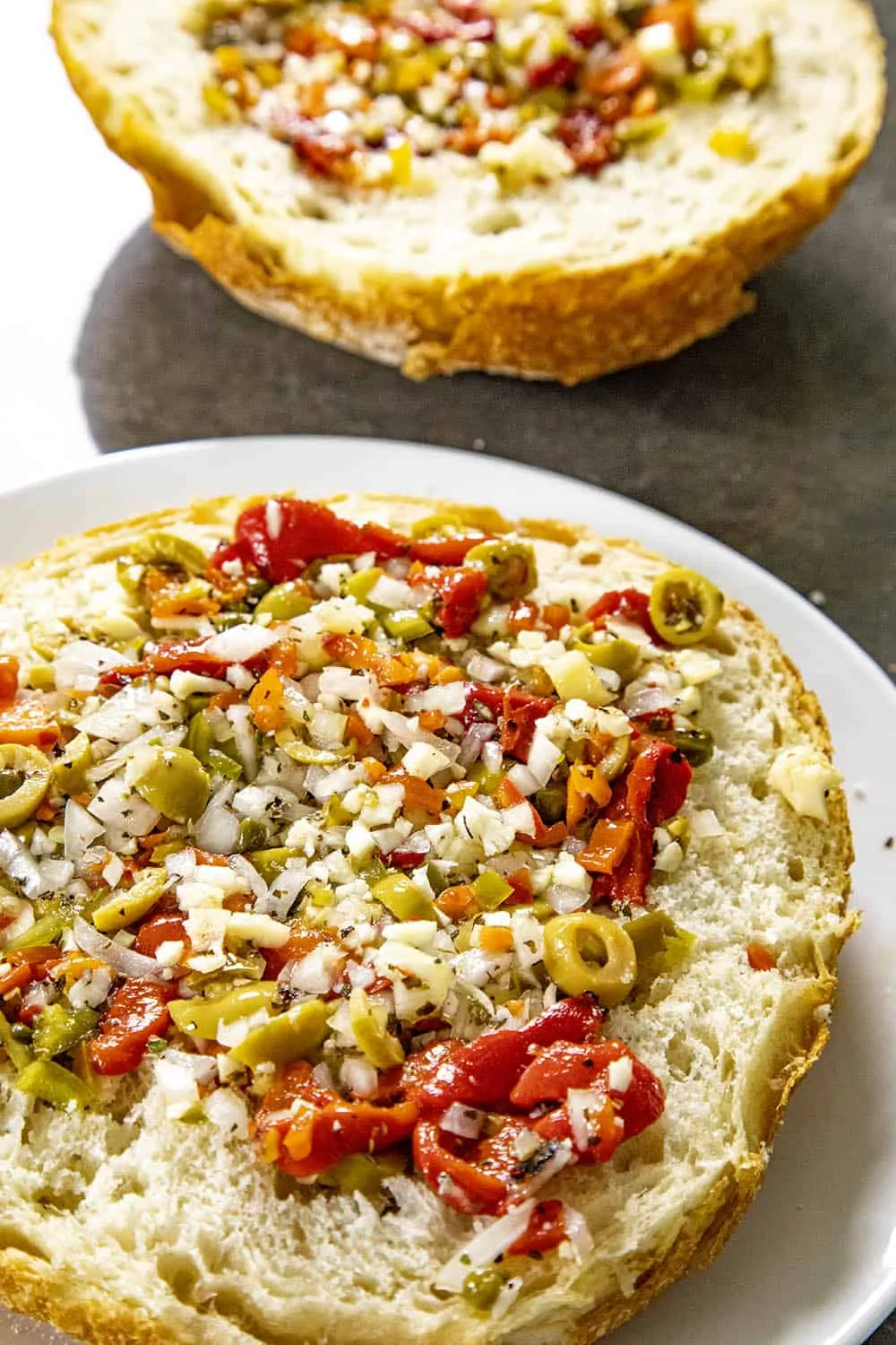 Olive tapenade being spread out over sliced Italian bread