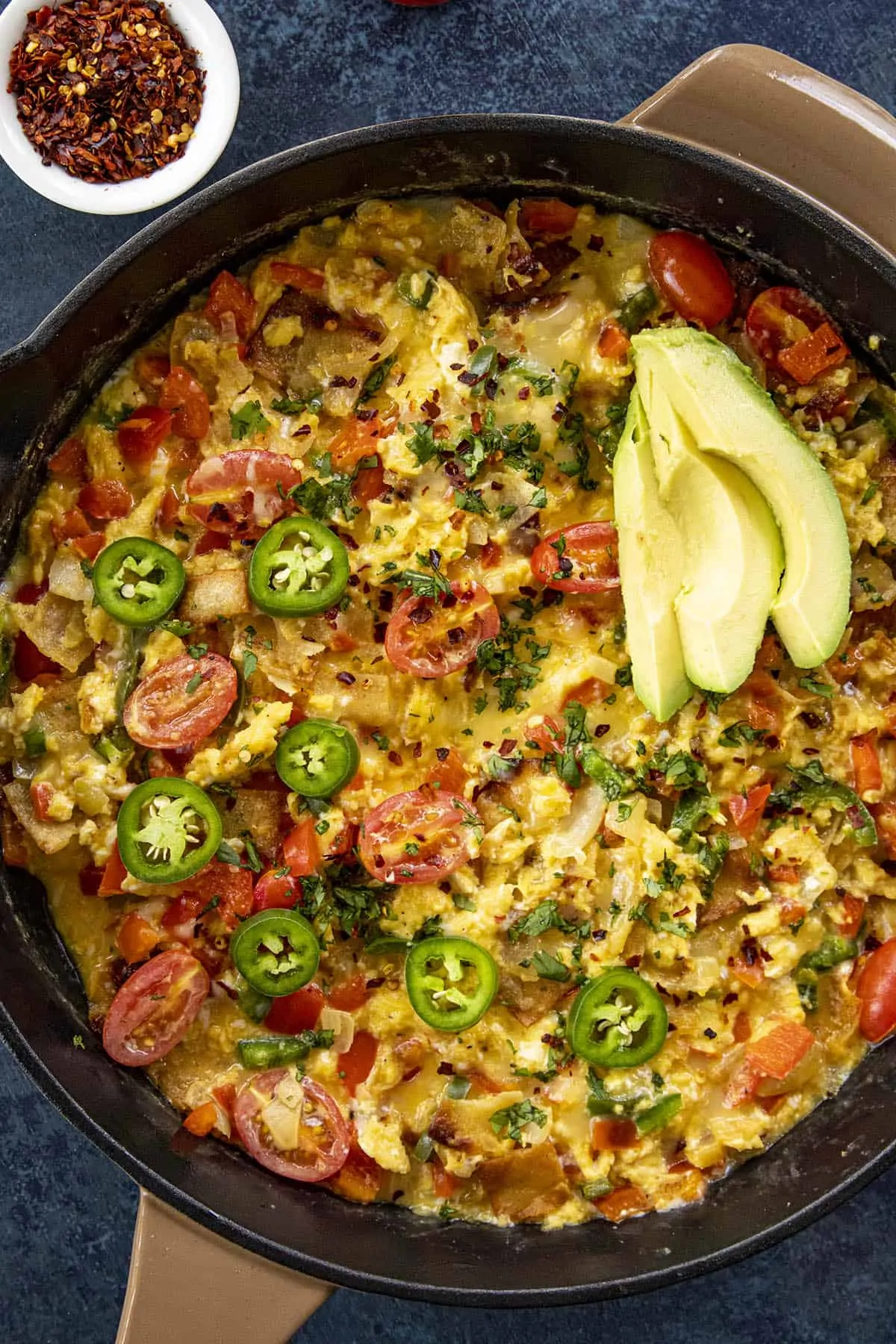 A big pan of Migas (Easy Mexican Scrambled Eggs with Crispy Tortillas), with avocado slices, sliced peppers, tomatoes and more