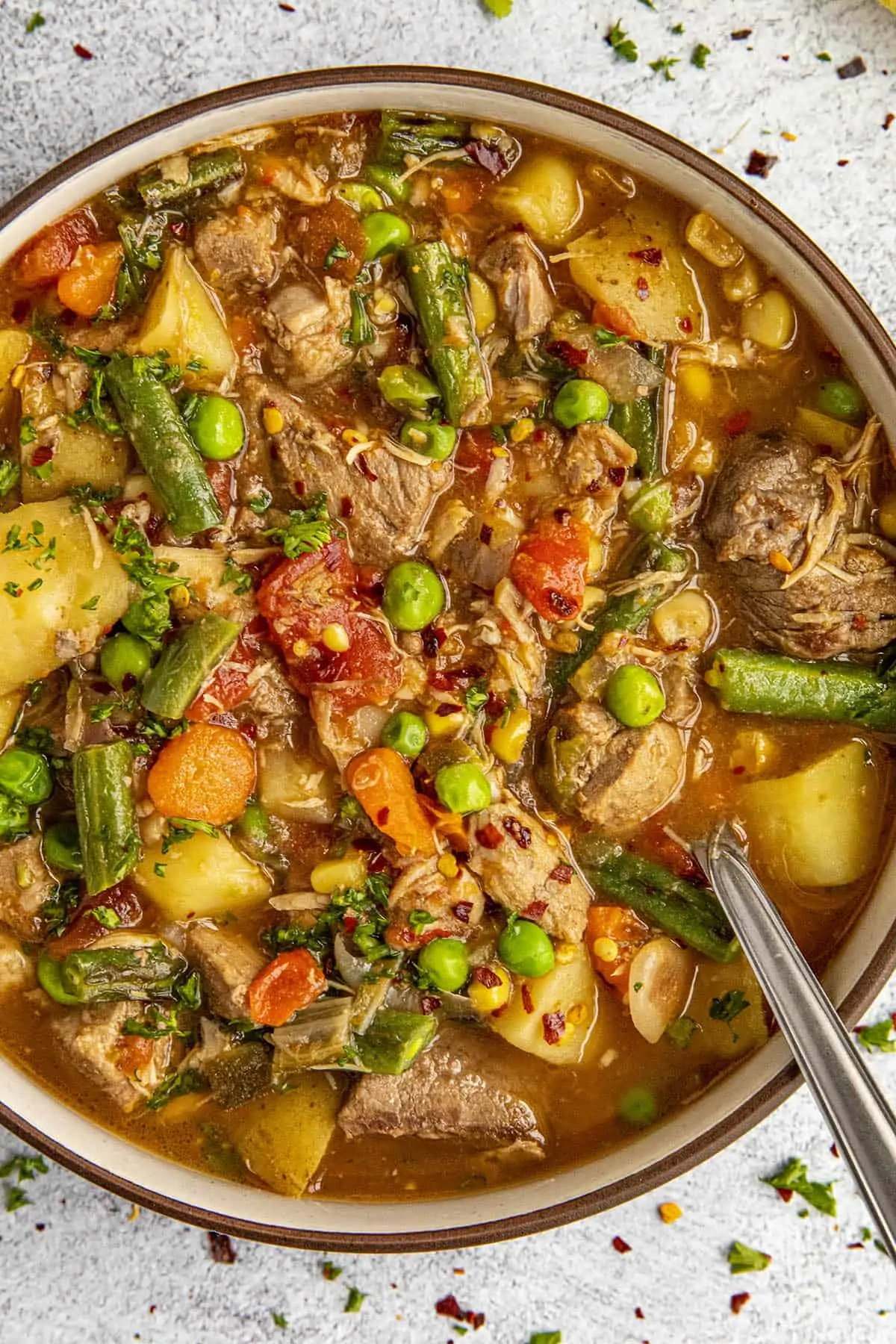 Chunky booyah stew in a bowl with a spoon, ready to enjoy