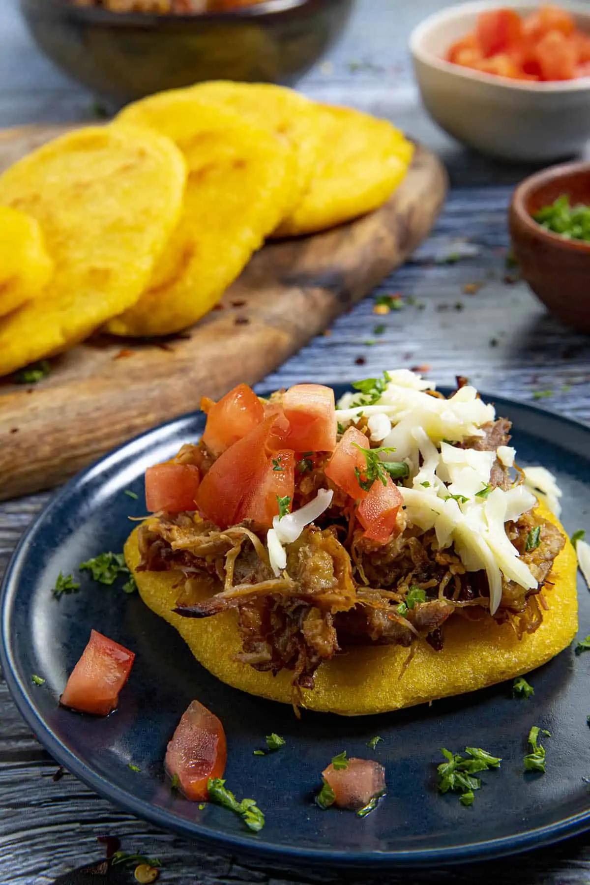 An arepa topped with pulled pork, shredded cheese and tomatoes