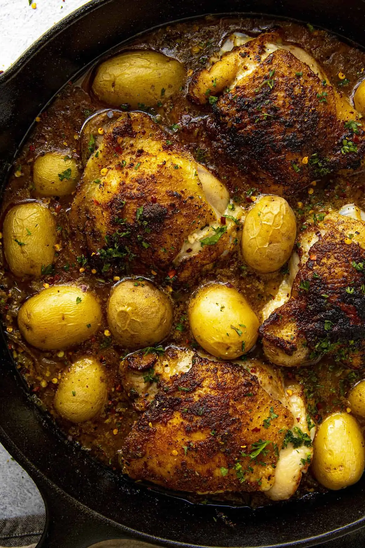 Spicy Baked Chicken Thighs seasoned with Cajun seasonings in a hot pan with potatoes
