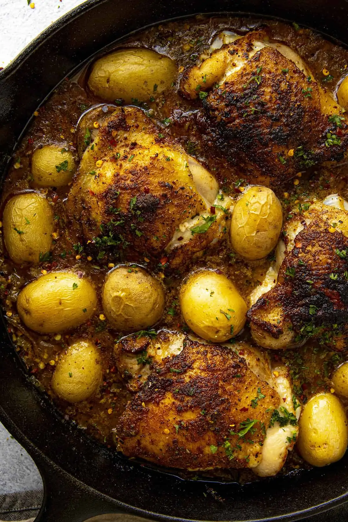 Spicy Baked Chicken Thighs seasoned with Cajun seasonings in a hot pan with potatoes.