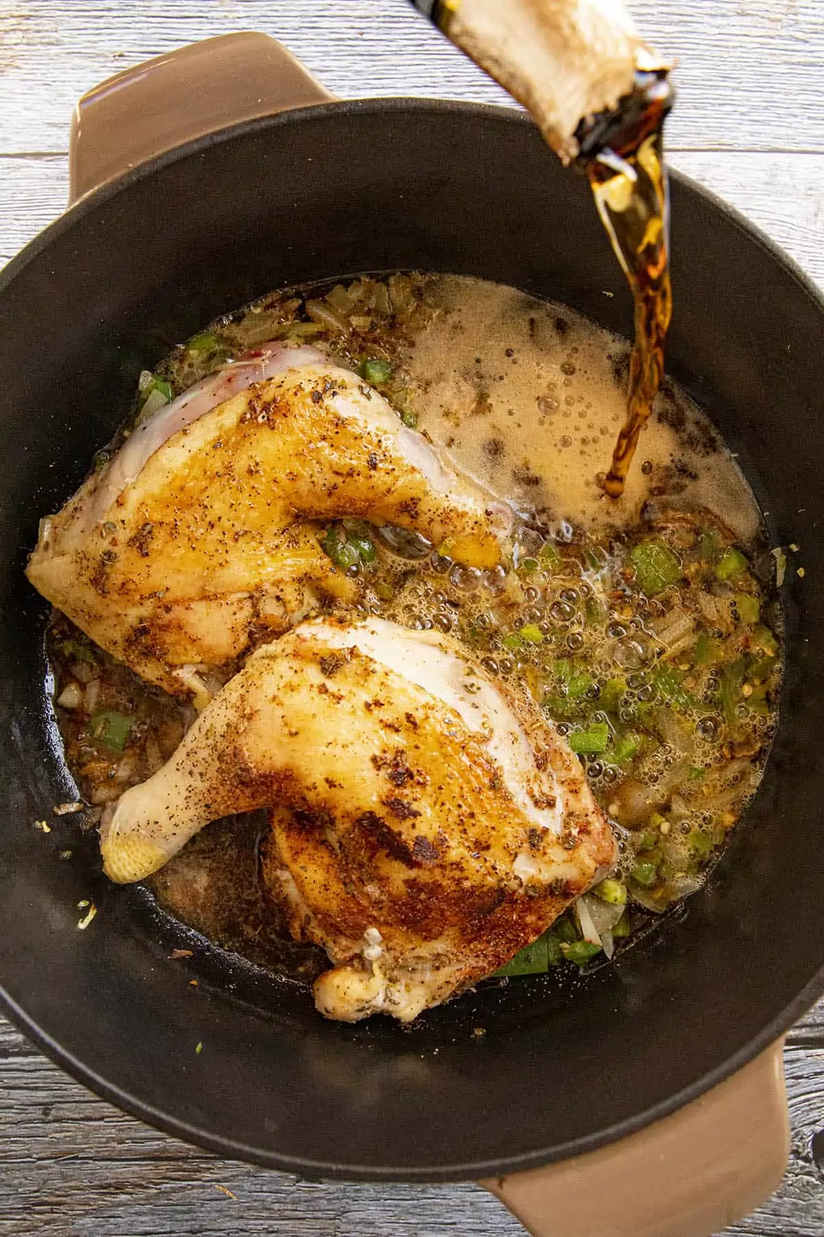 Adding liquid to the pan to braise the chicken.