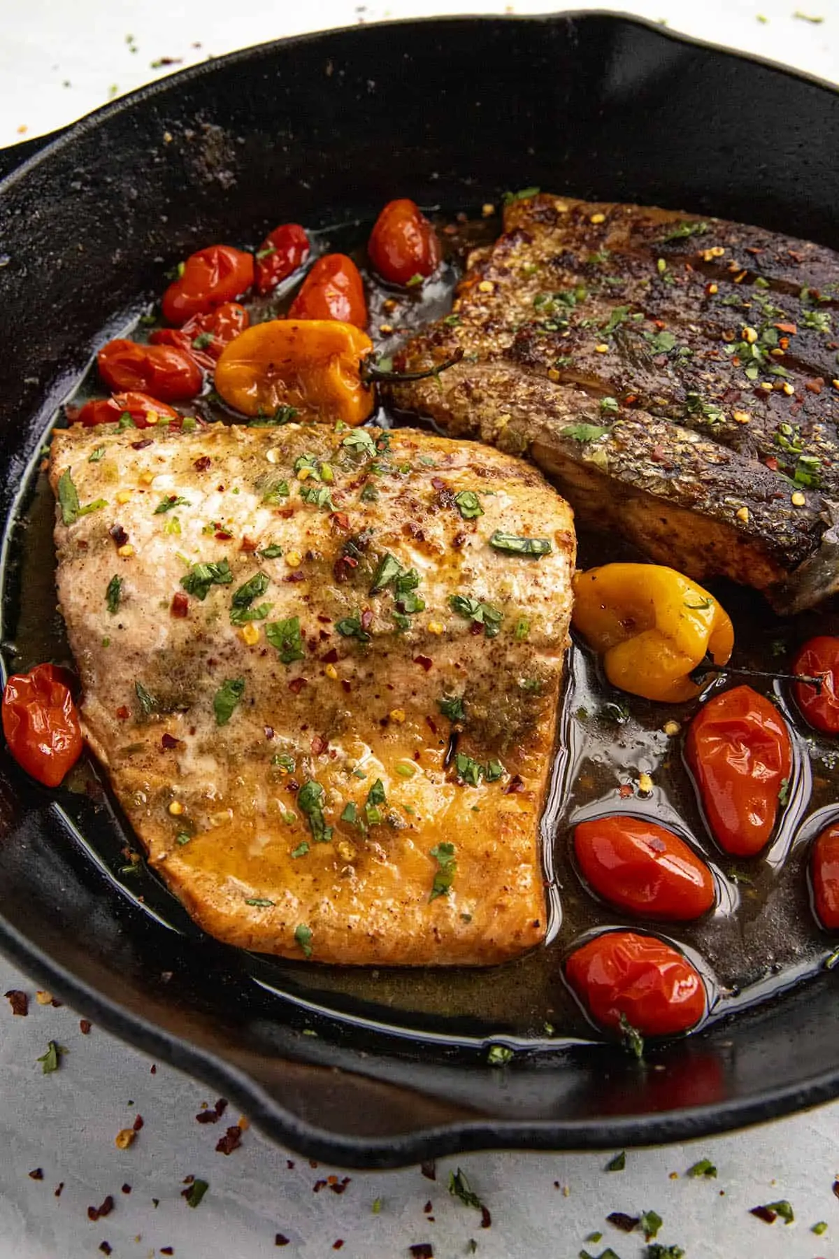 Two pieces of Jerk Salmon in a hot pan with blistered tomatoes and Scotch Bonnet.