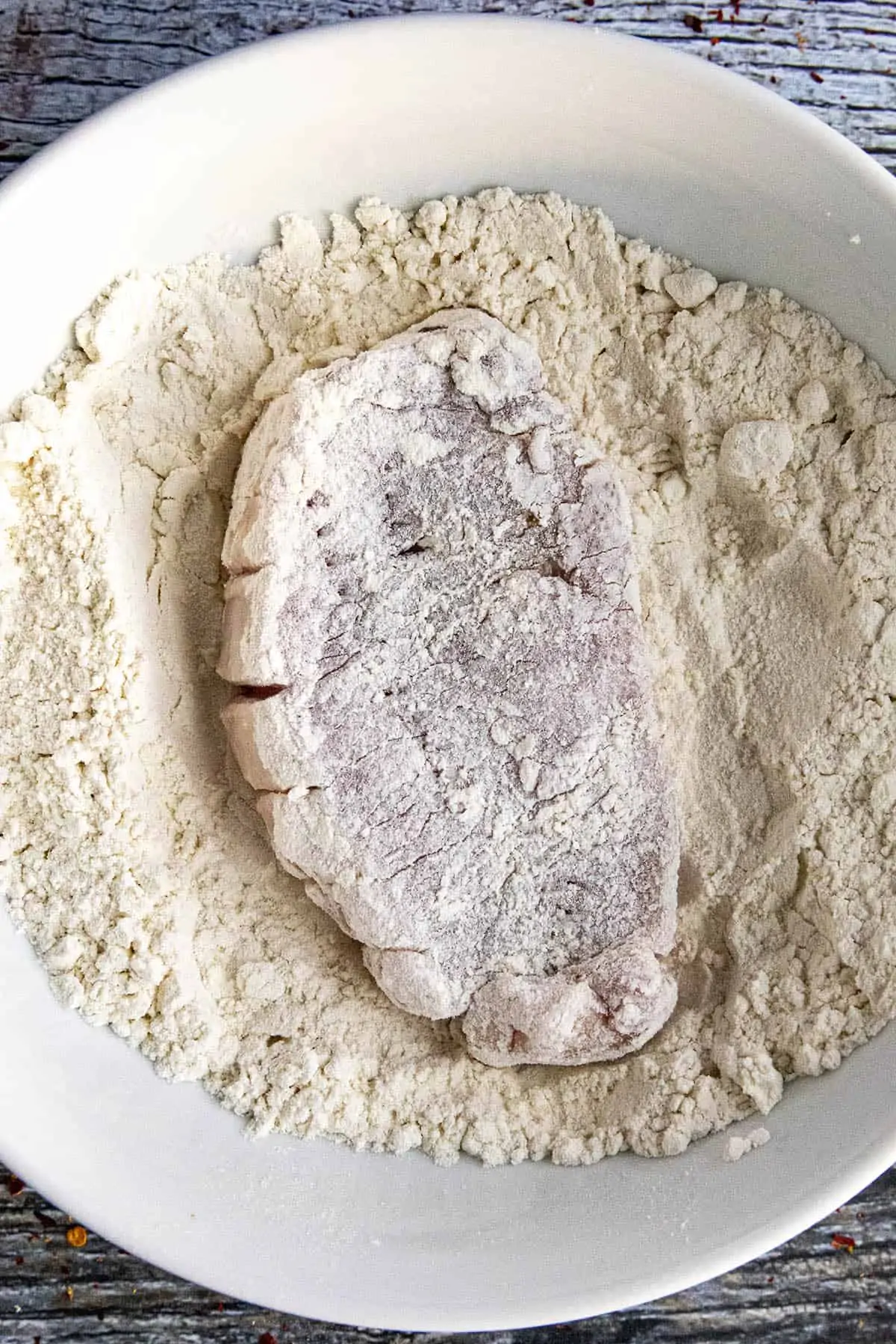 Coating the pork cutlet in flour.