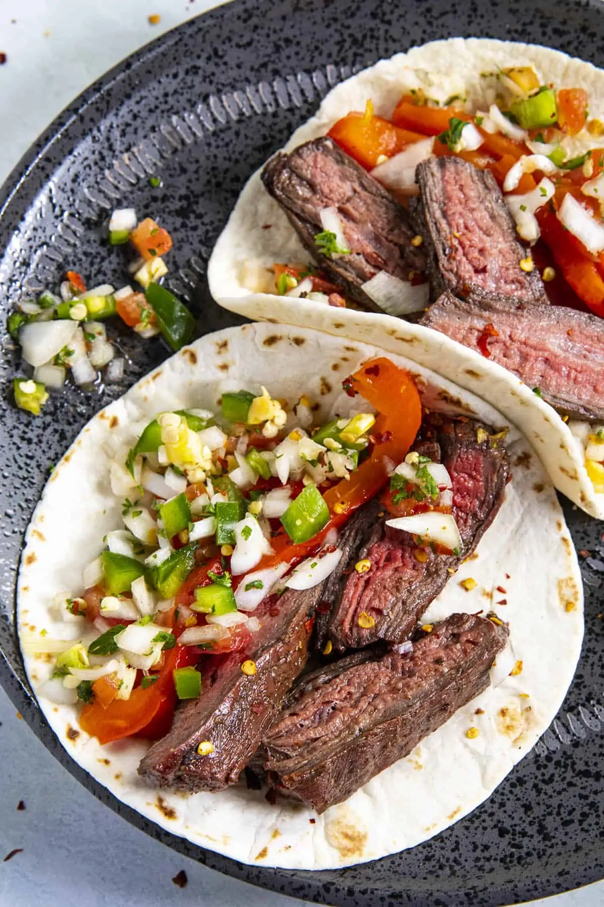 Two charcoal grilled steak tacos with pico de gallo and grilled red pepper.