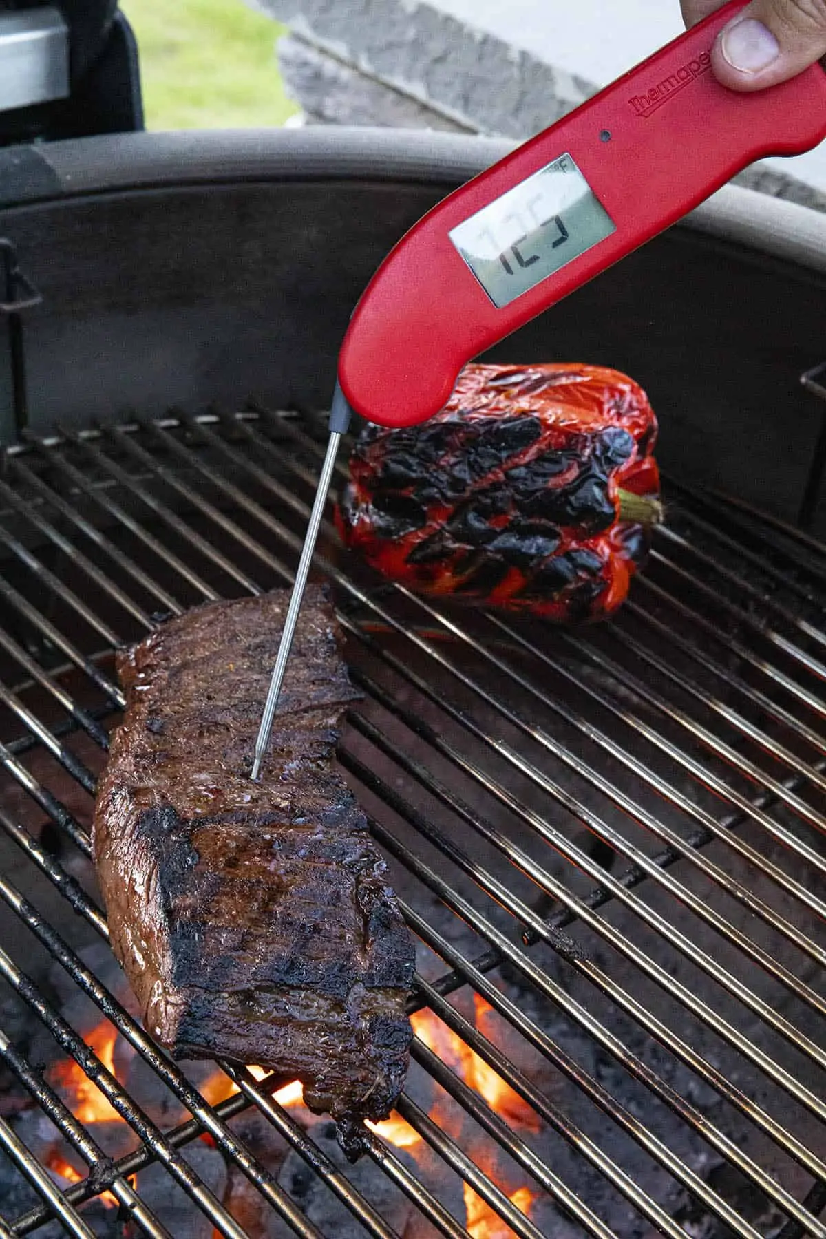 Checking the internal temperature of the flank steak on the grill with a meat thermometer.