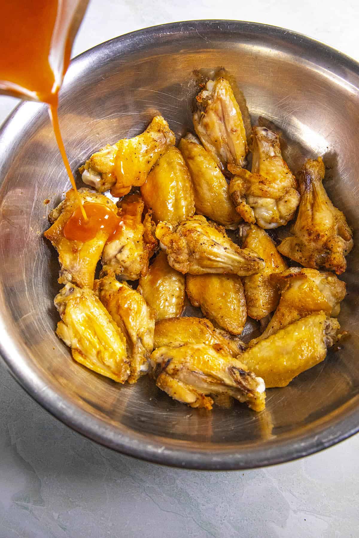 Pouring homemade Buffalo sauce over hot Buffalo wings