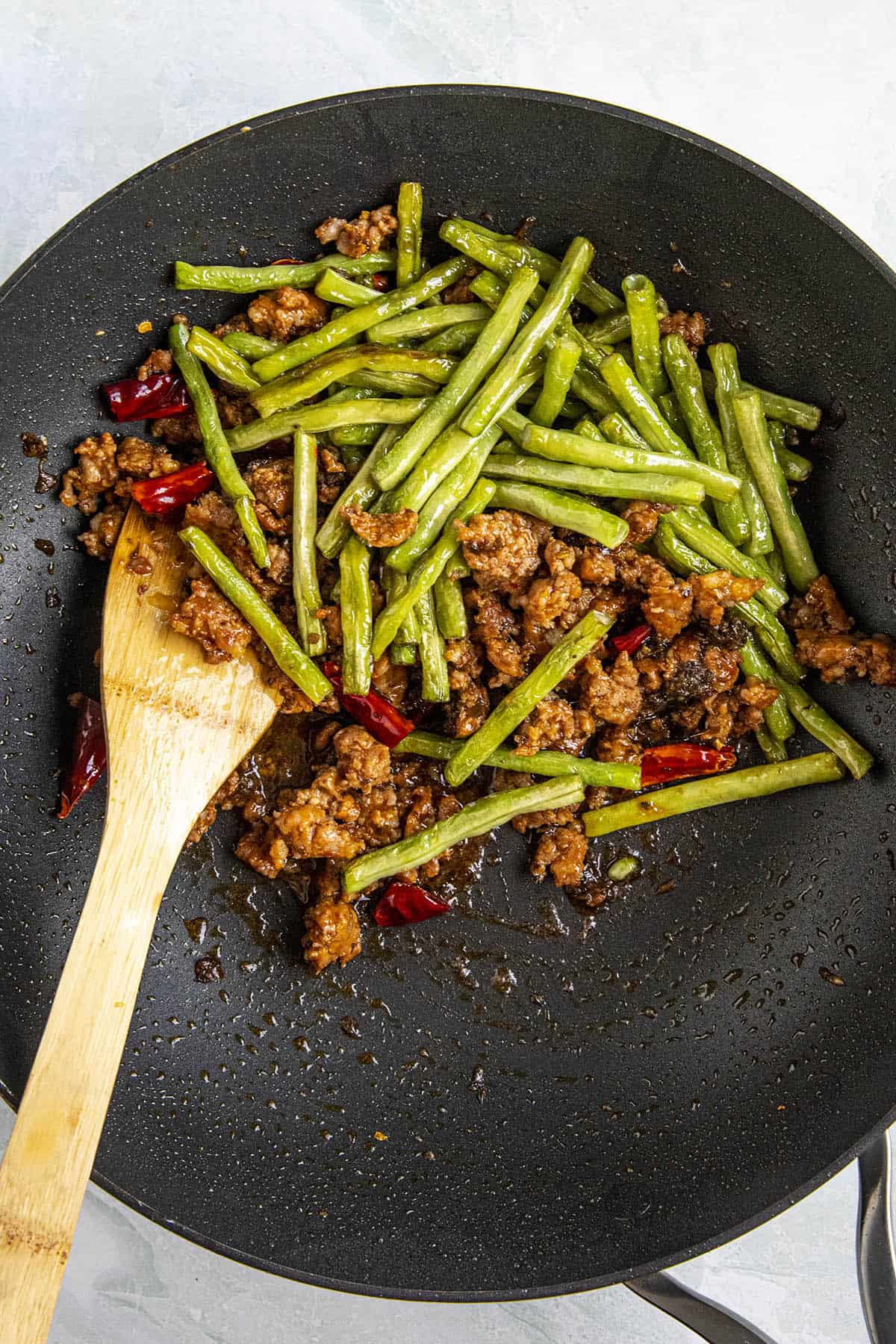 Stirring together the long beans with the pork and peppers in a hot pan