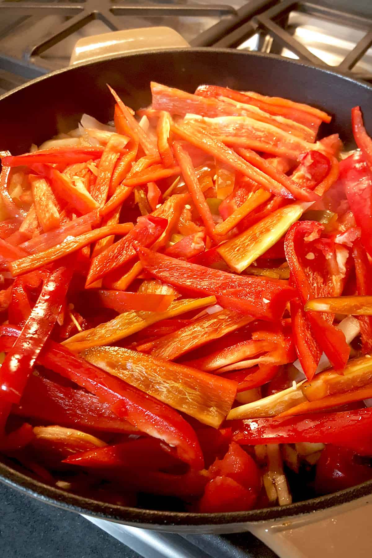 Cooking down bell peppers and onion in a pan with oil to make Peperonata