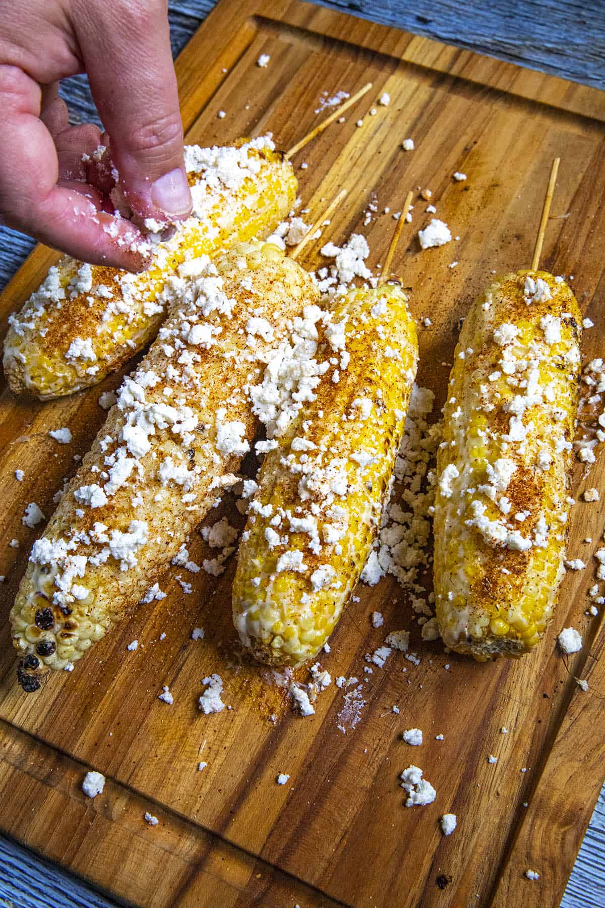Coating the grilled corn with crumbly white cheese