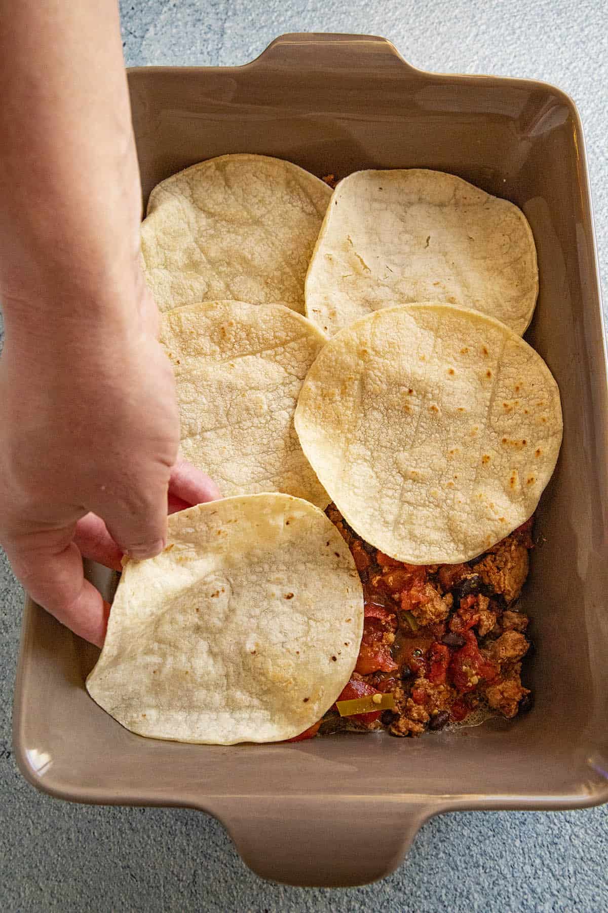 Spreading corn tortillas onto the Mexican Lasagna