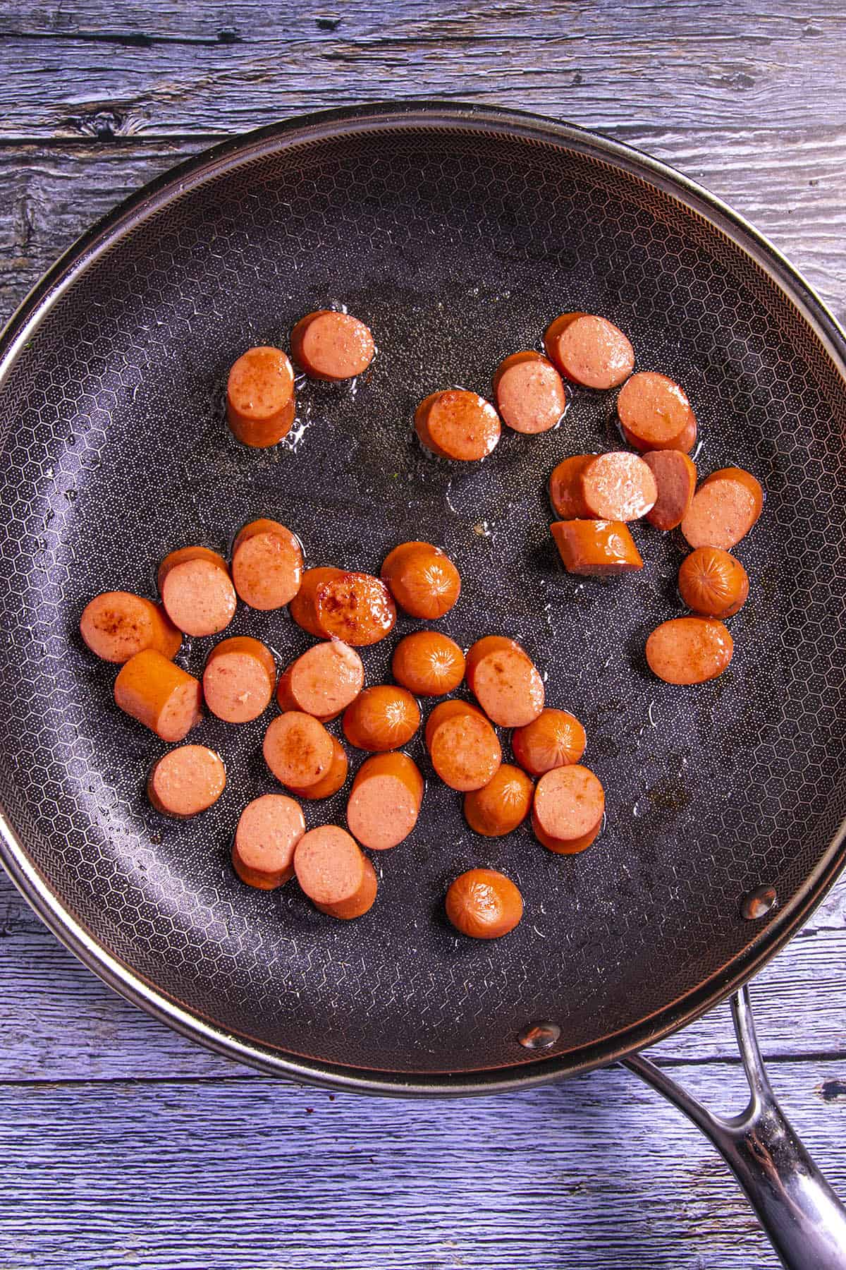 Cooking beef sausages in a pan to make Salchipapas