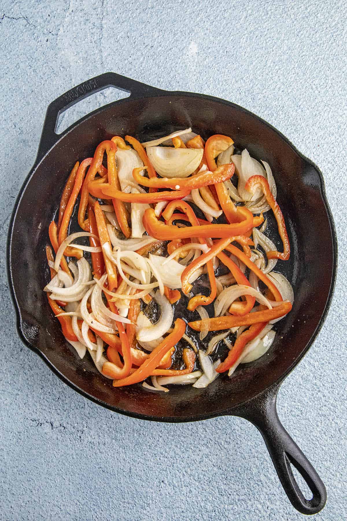 Peppers and onions cooking down in a cast iron pan