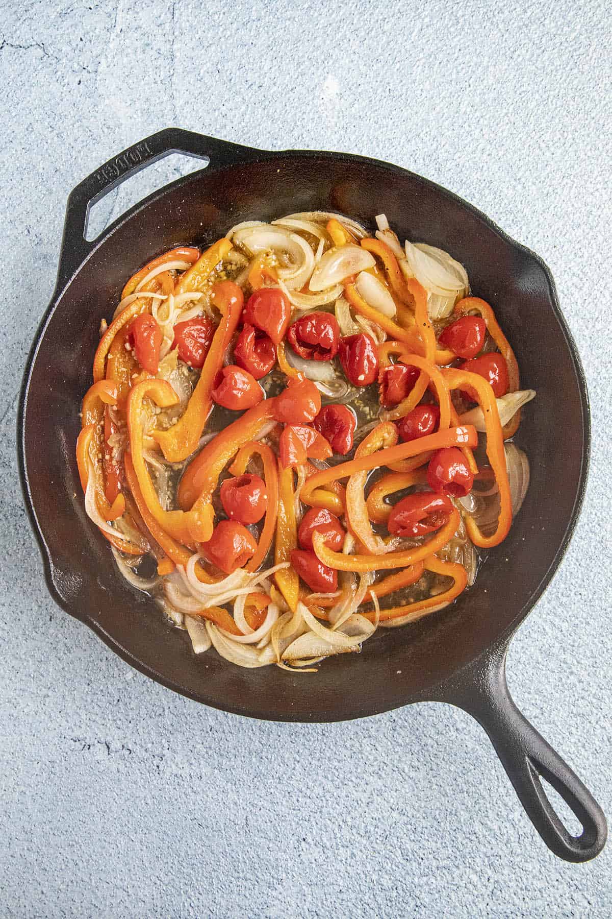 Pickled peppers added to the hot pan with bell peppers and onions