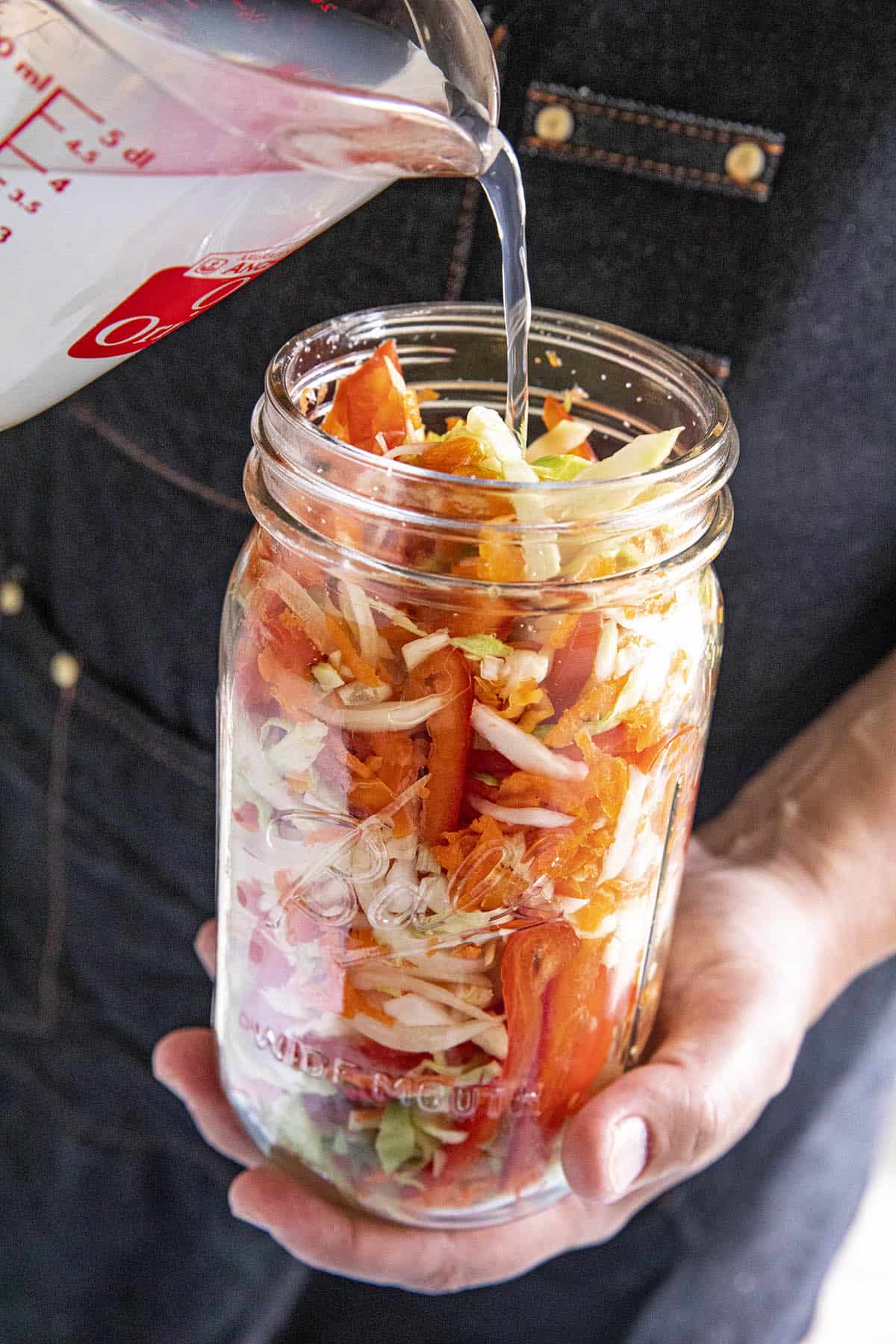 Pouring the brine into the jar of vegetables to make Pikliz