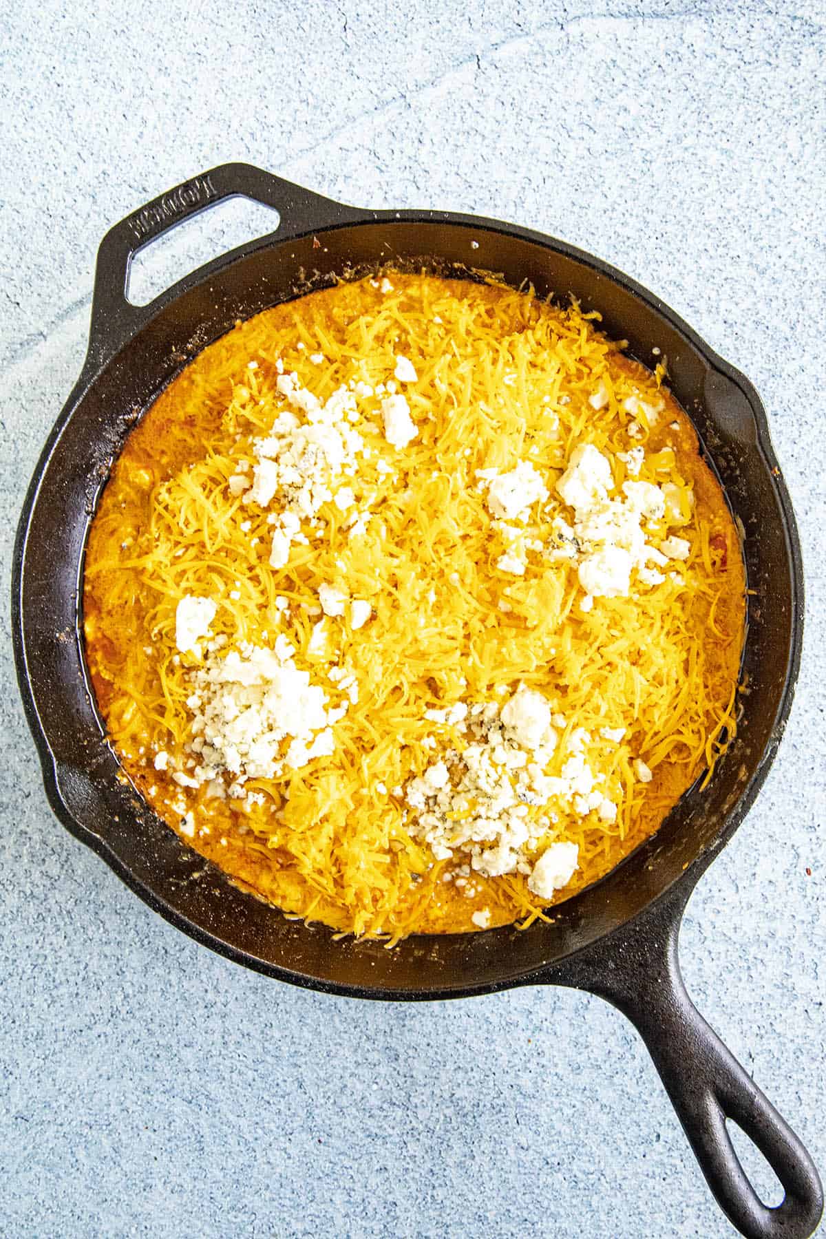 Topping the Buffalo Chicken Dip with shredded cheddar cheese