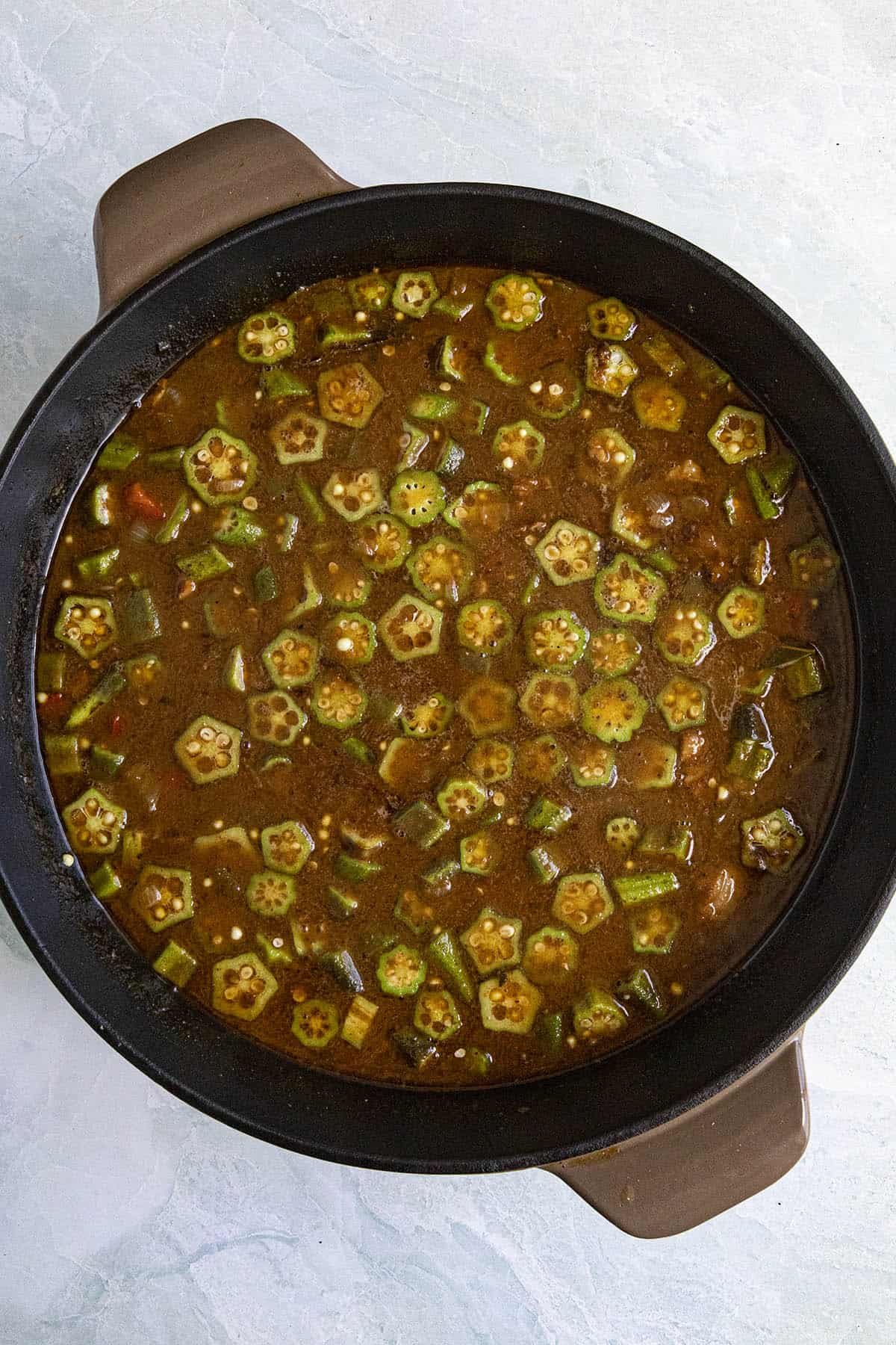 Adding sliced okra to the pot of simmering gumbo