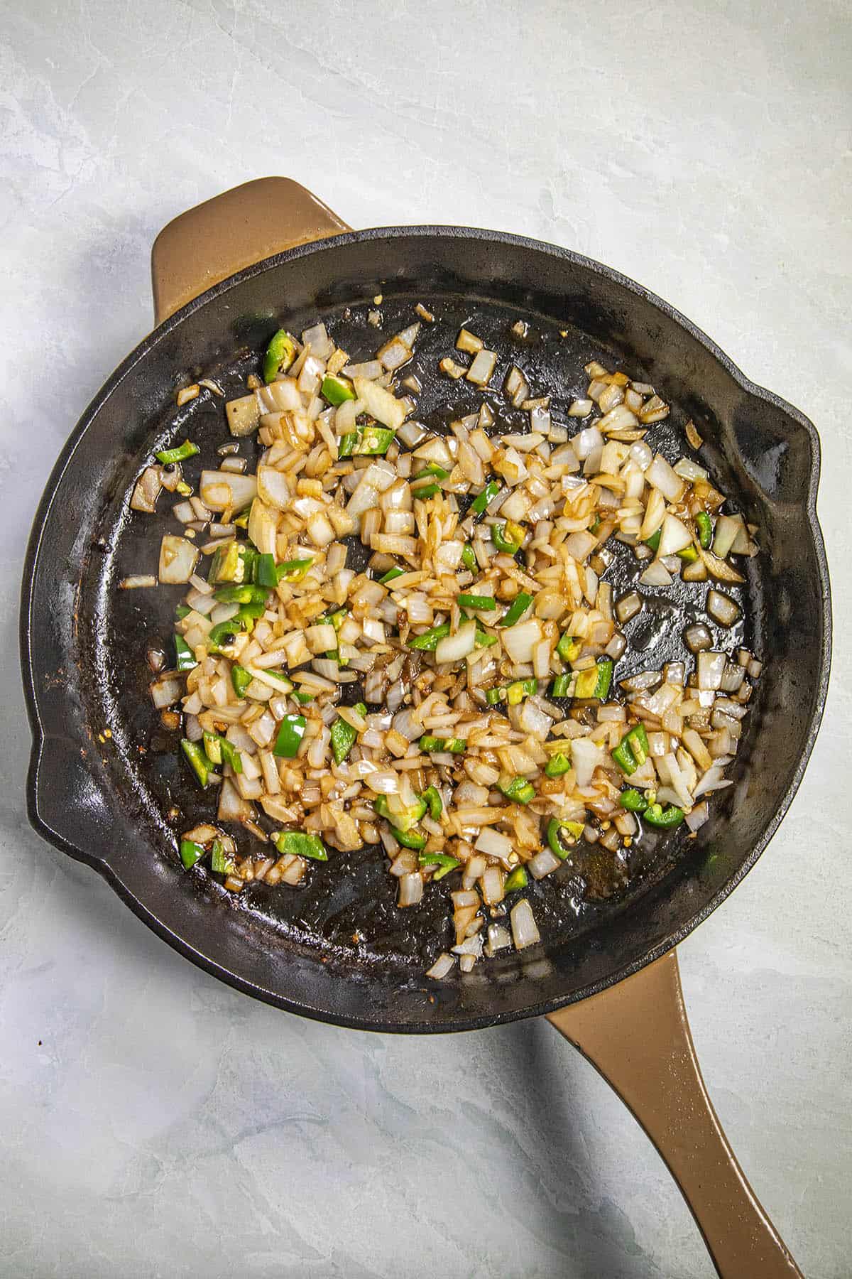 Cooking down peppers and onions in a pan to make Chicken Adobo