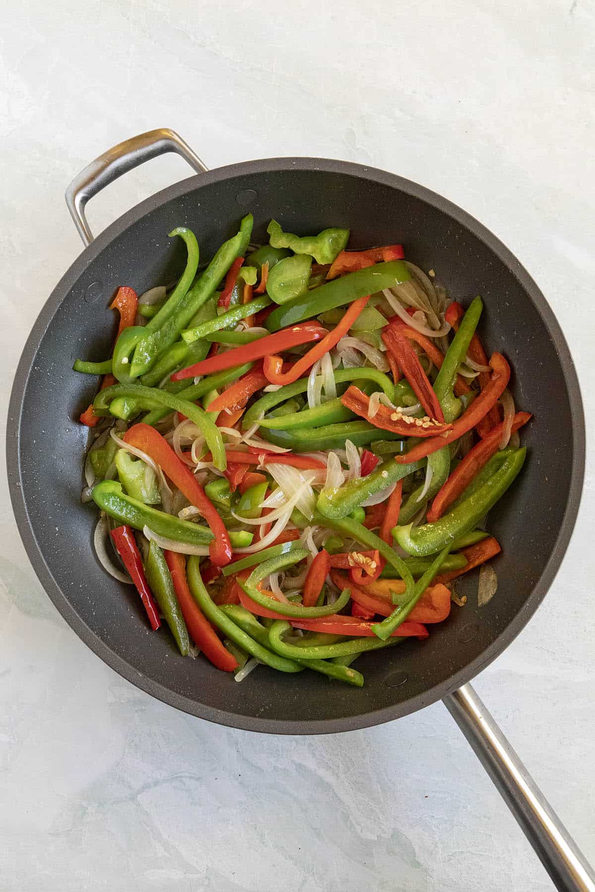 Cooking peppers and onions in a pan to make Piperade
