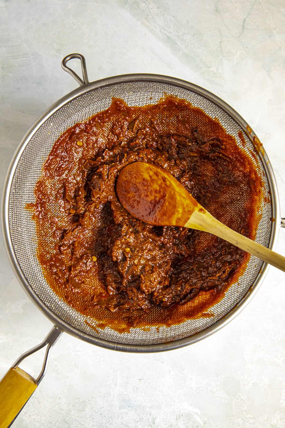 Straining red chili sauce into a bowl for Pozole Rojo