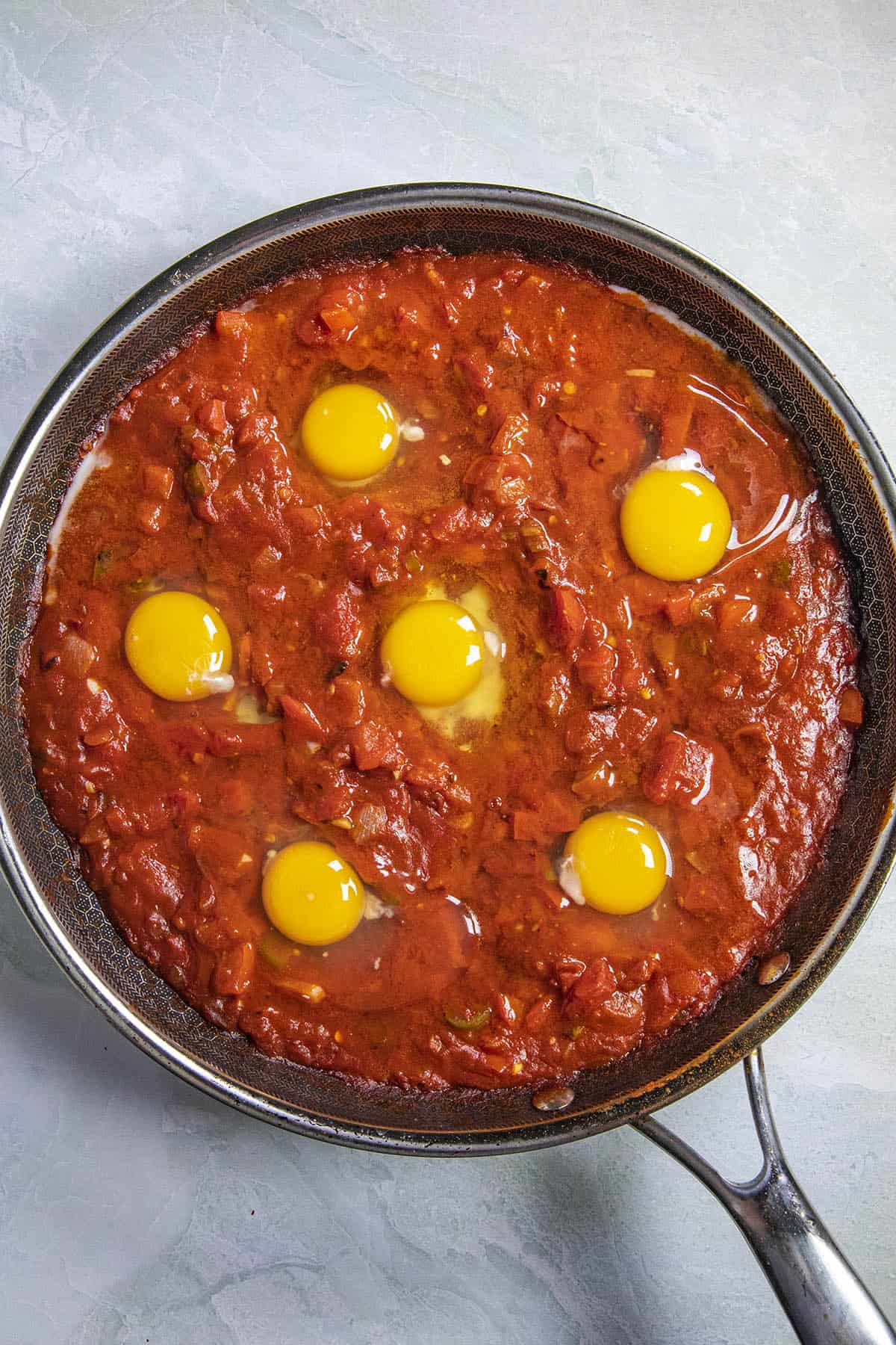 6 eggs cracked into spicy tomato sauce to make Shakshuka
