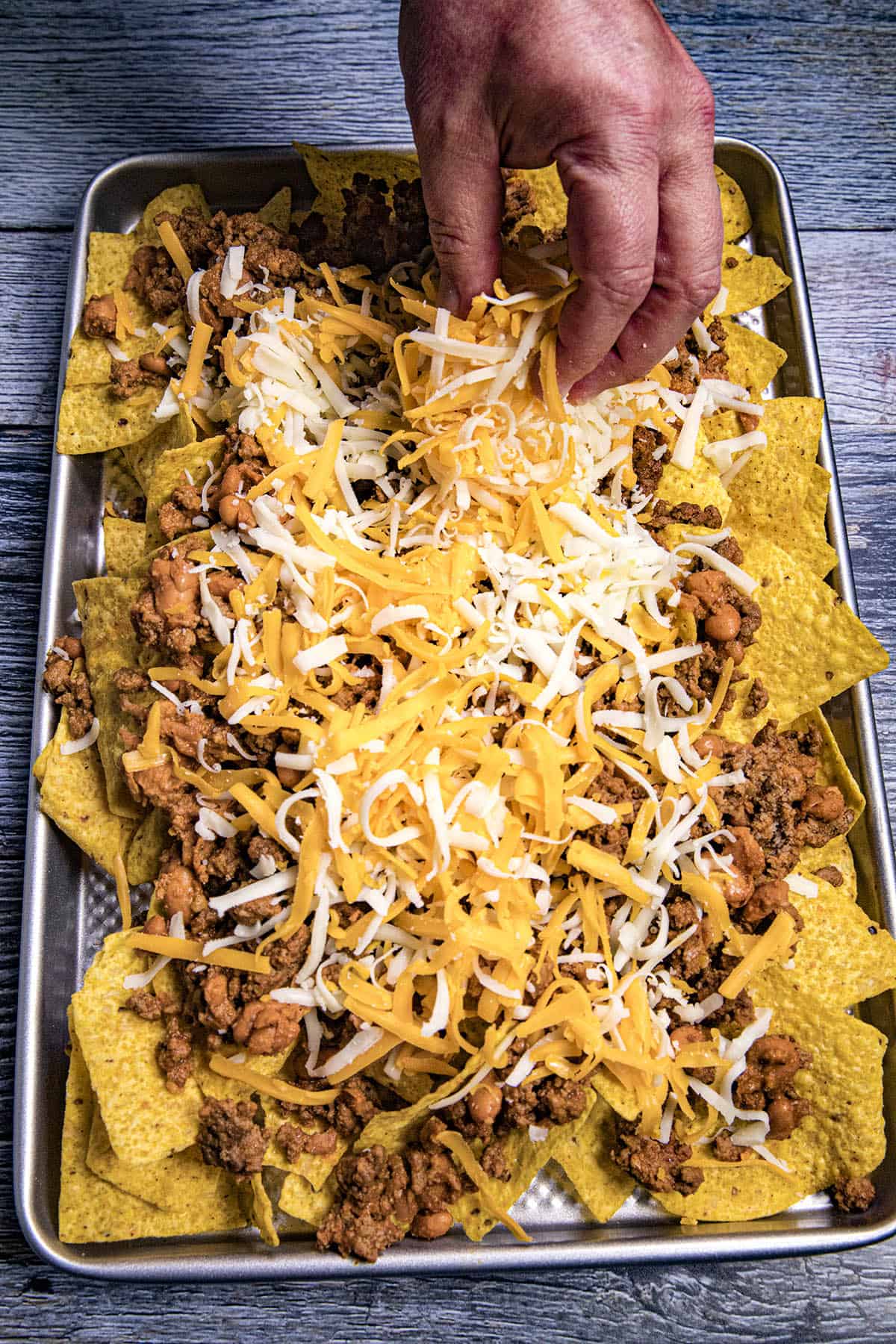 Mike layering shredded cheese onto the nachos base