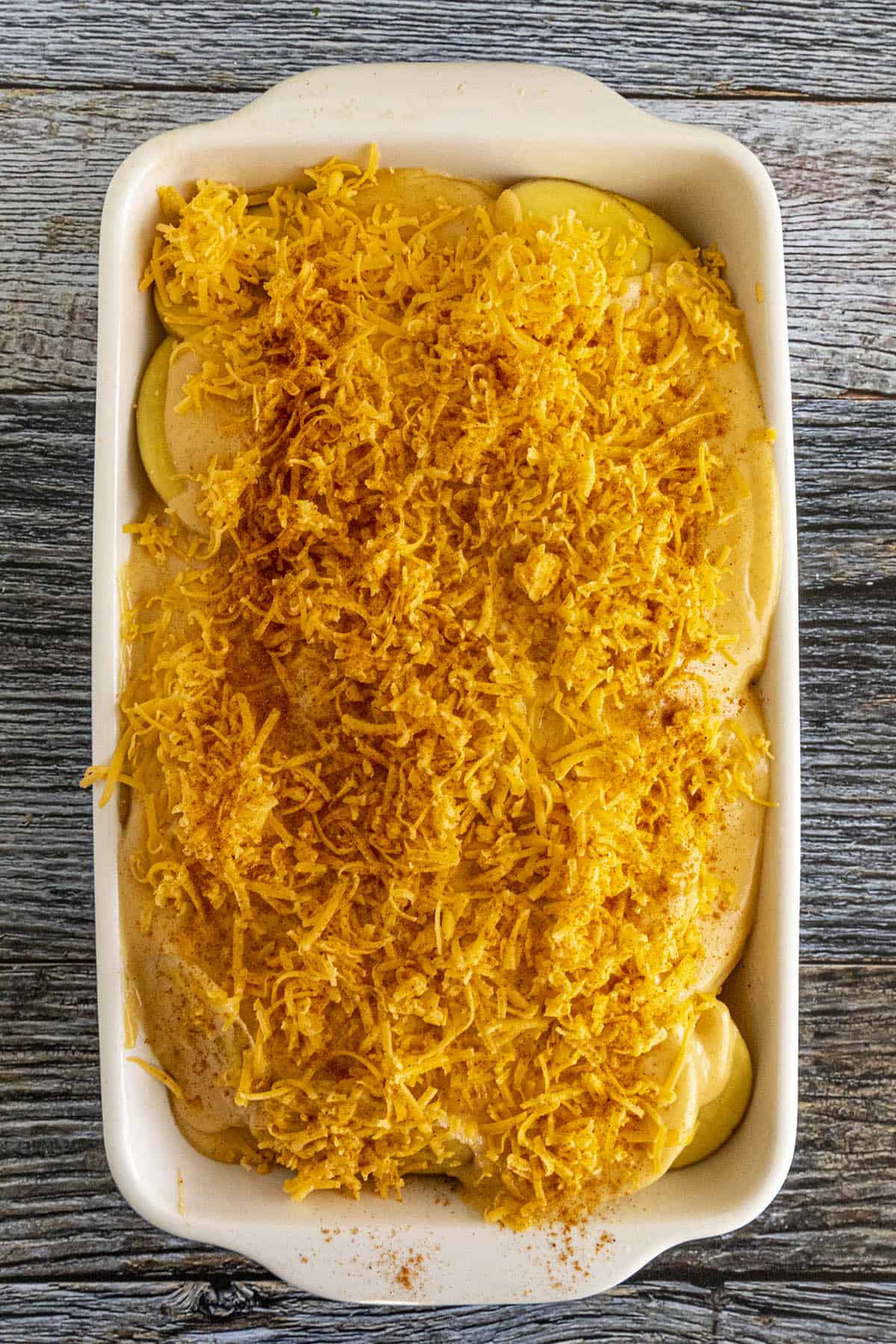 Scalloped Potatoes topped with shredded cheddar cheese, ready for the oven