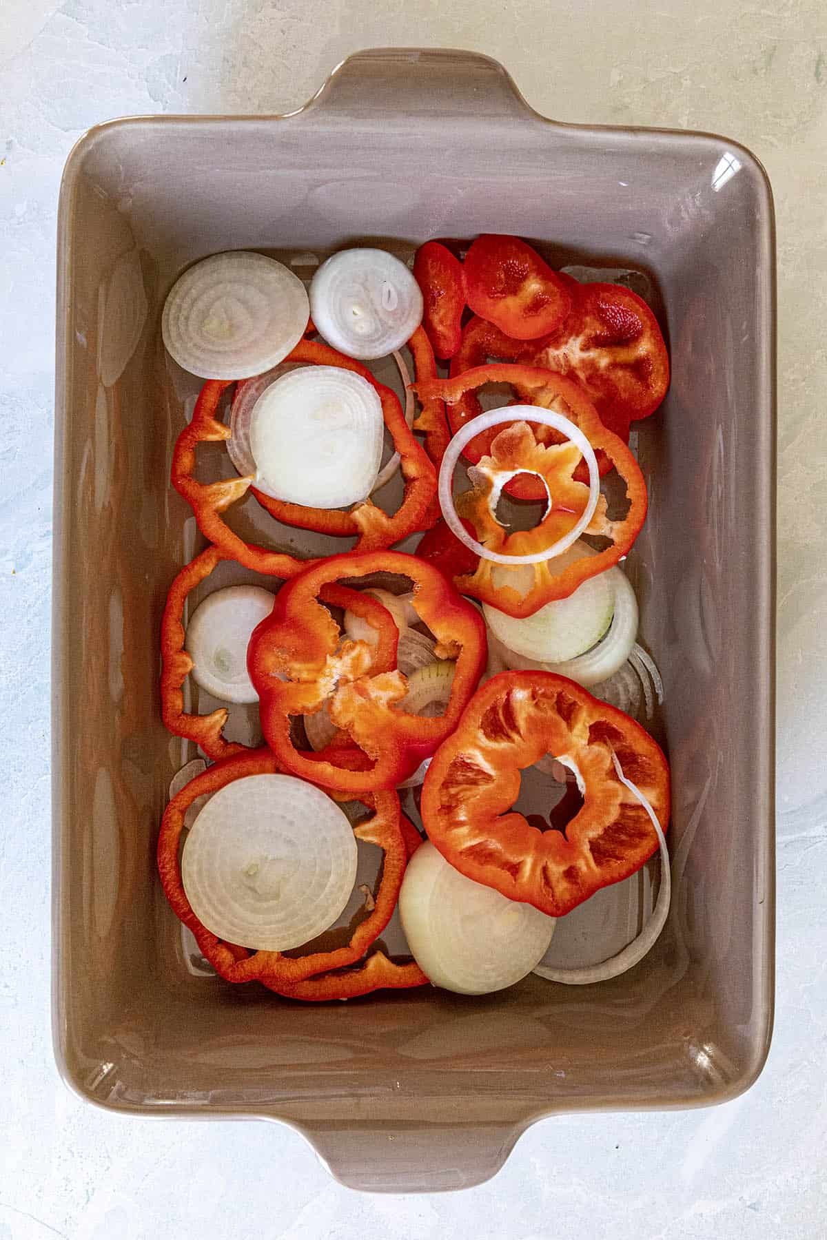 Peppers and onions layered into the bottom of a baking dish