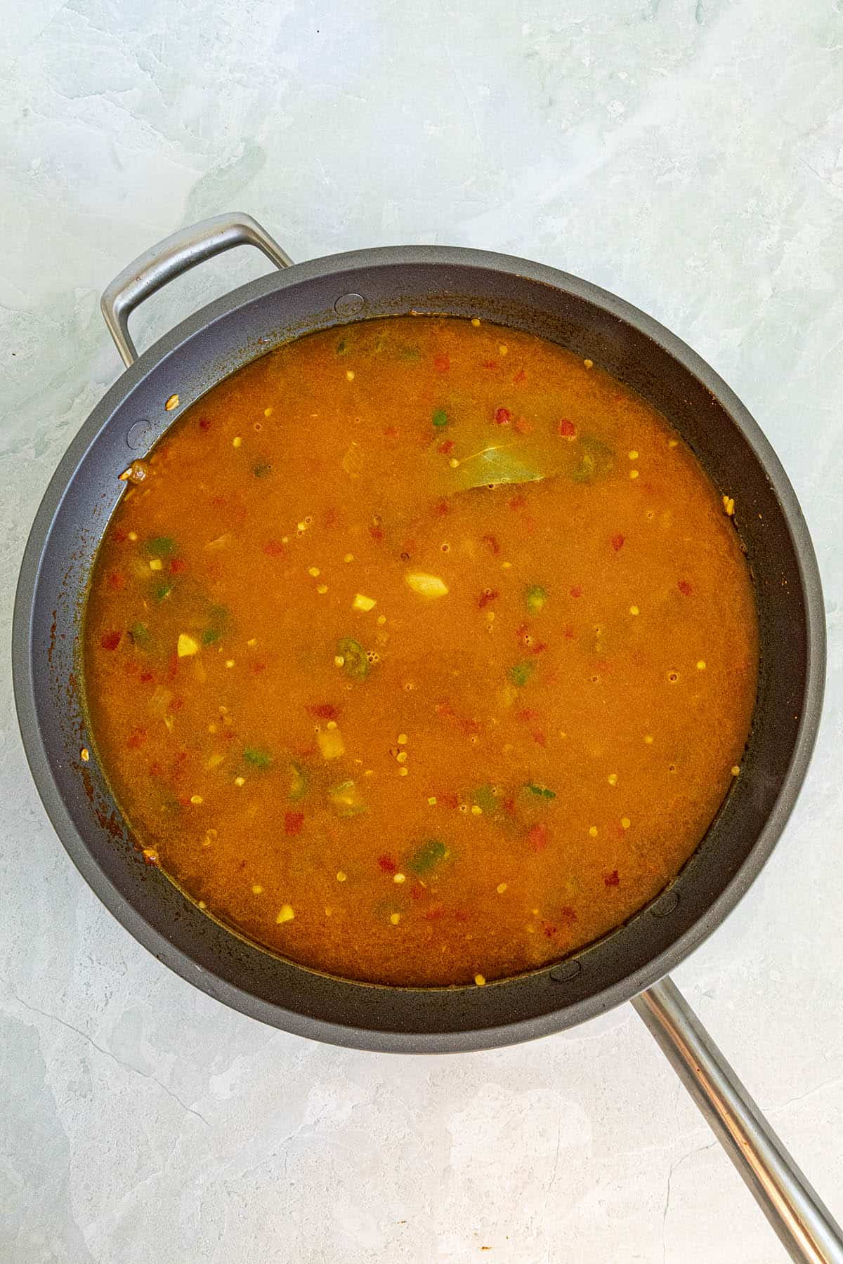 Yellow rice in pan with liquid and seasonings, ready for simmering