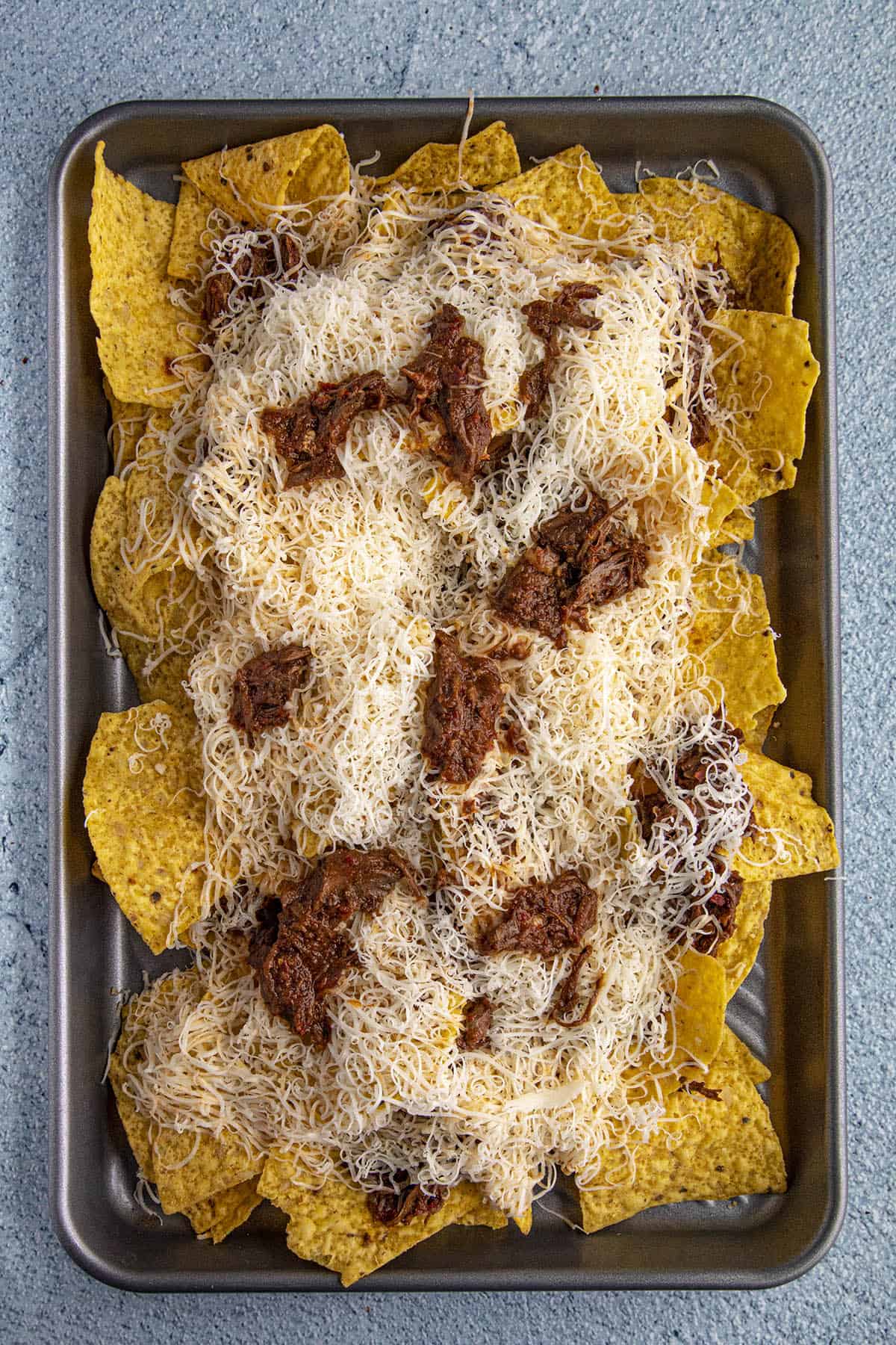 Birria Nachos ready for the oven, with lots of shredded cheese