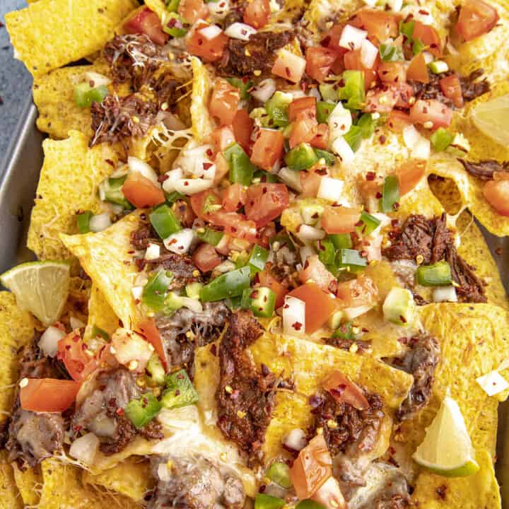 Birria Nachos on a serving platter with birria consome for dipping