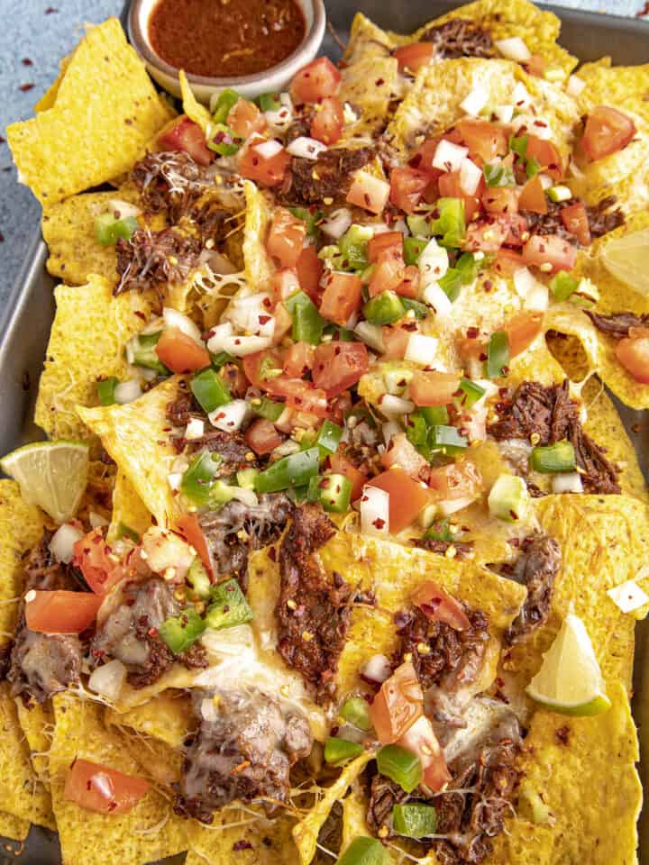 Birria Nachos on a serving platter with birria consome for dipping