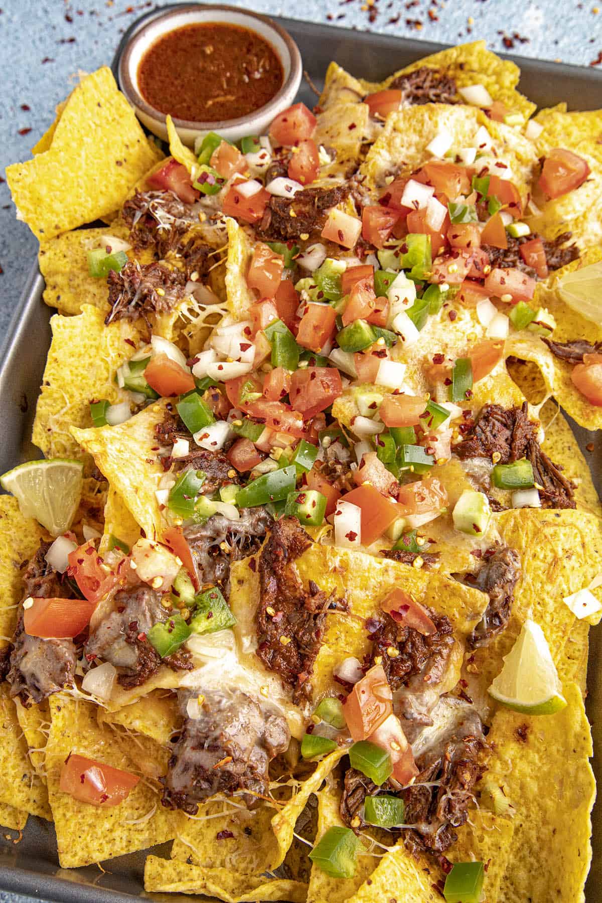 Birria Nachos on a serving platter with birria consome for dipping