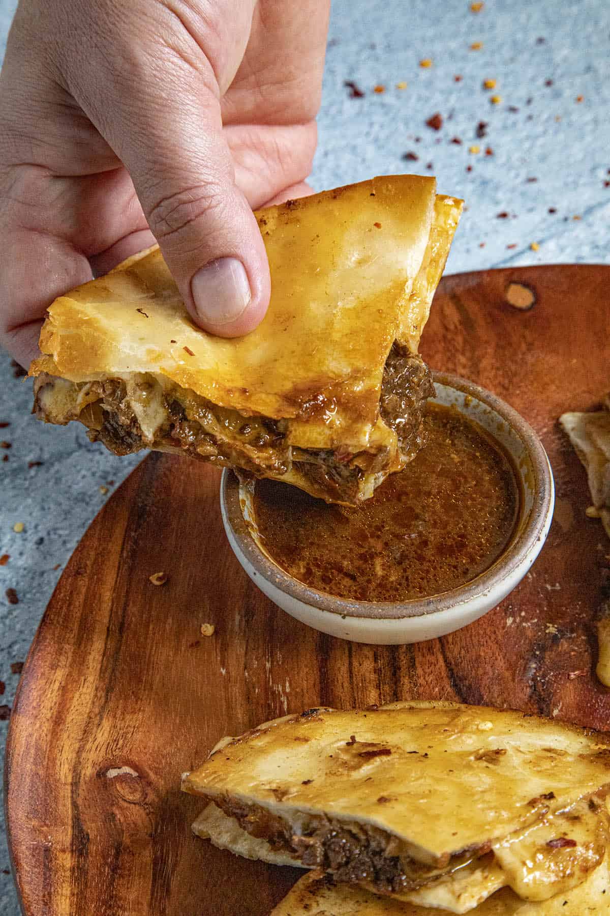 A cheesy Birria Quesadilla being dunked into birria sauce (consome)