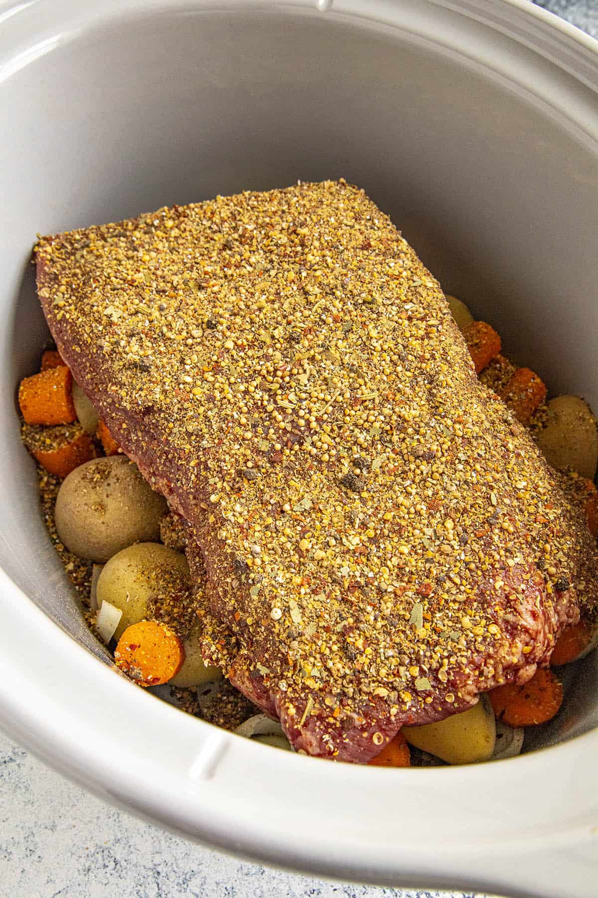 Highly seasoned corned beef in a crock pot, ready for slow cooking