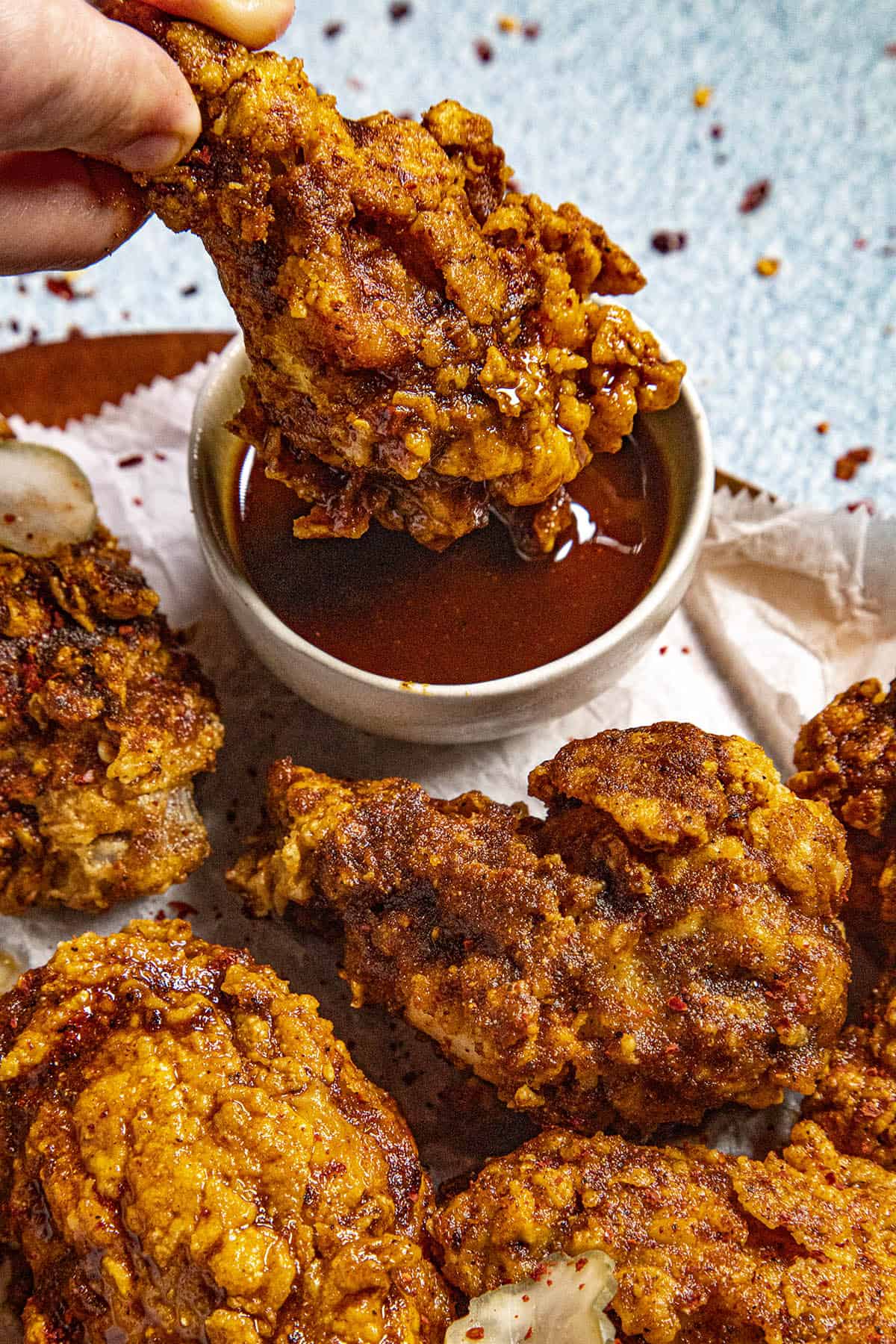 Dipping a piece of crispy fried chicken into a bowl of Nashville Hot Sauce