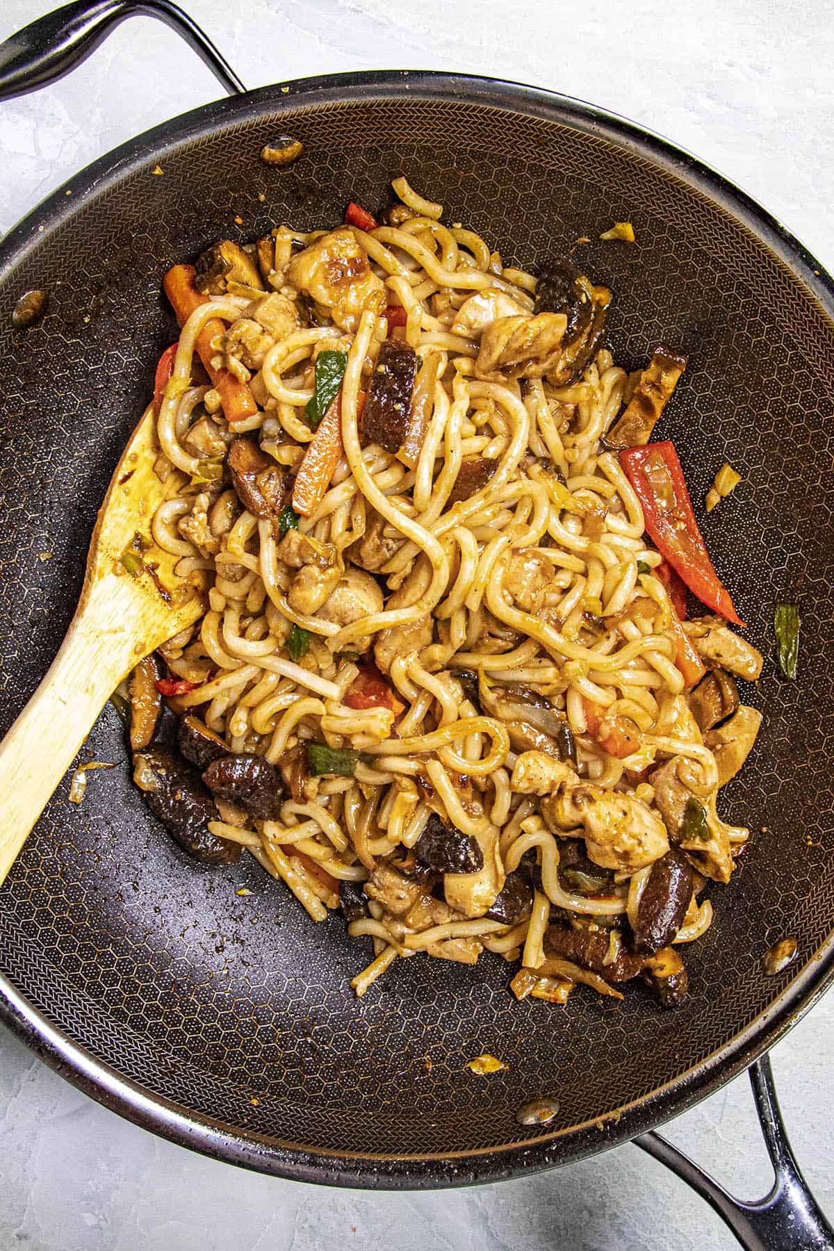 Stirring noodles and yaki udon sauce into the wok with vegetables