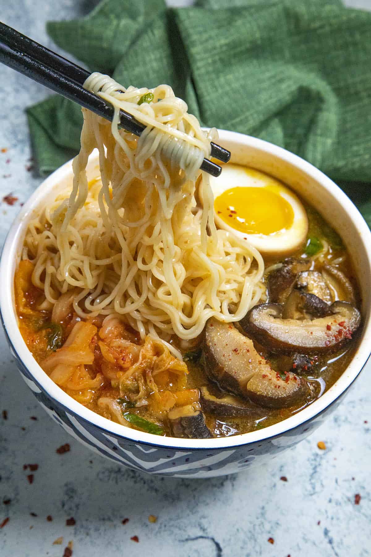 Lifting ramen noodles with chopsticks from a big bowl of kimchi ramen