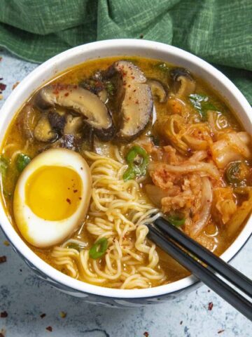 Spicy Kimchi Ramen in a bowl with lots of kimchi, mushrooms, and noodles, topped with a jammy soft boiled ramen egg