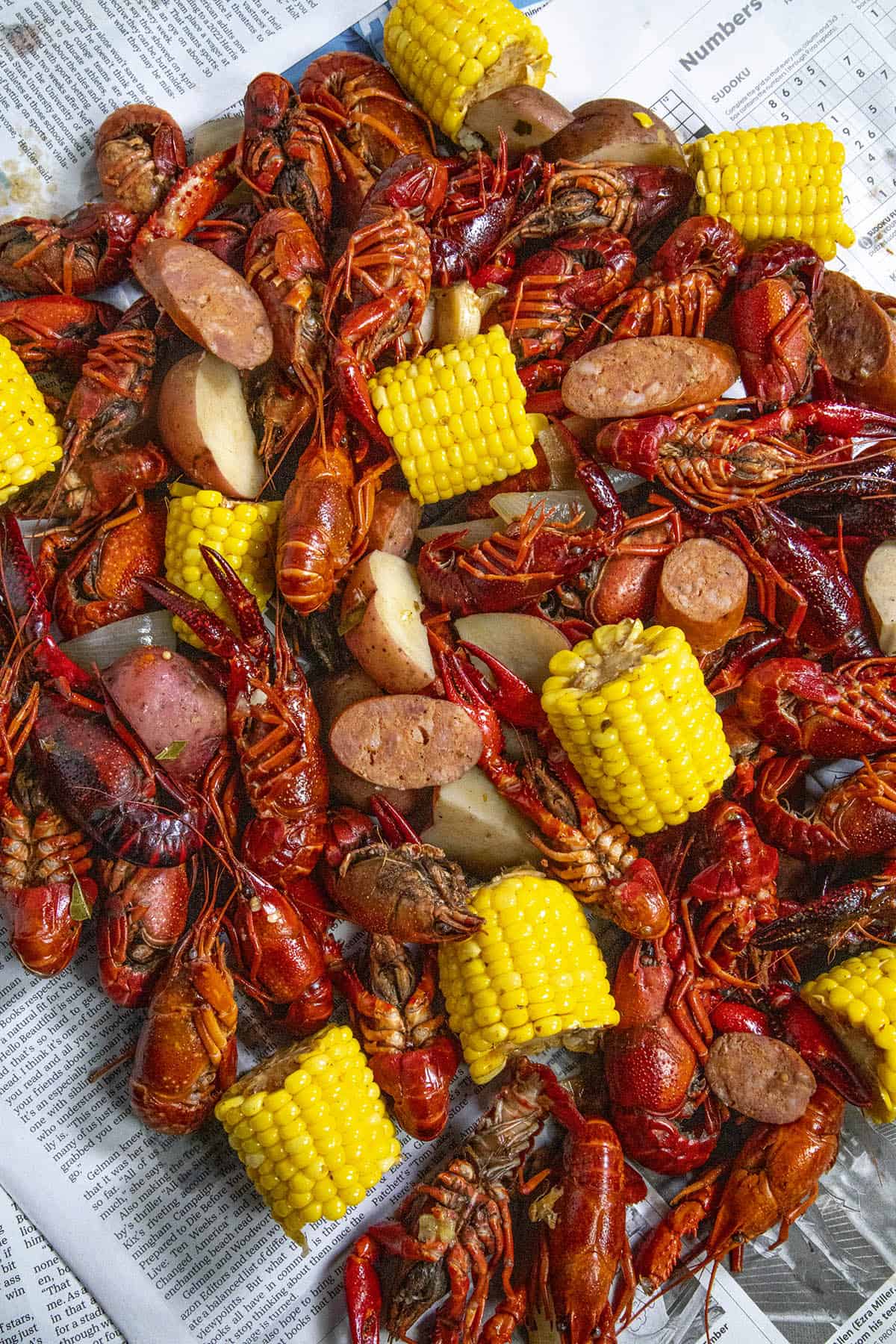 Lots of boiled crawfish, corn, potatoes, and andouille sausage piled over newspaper on a table
