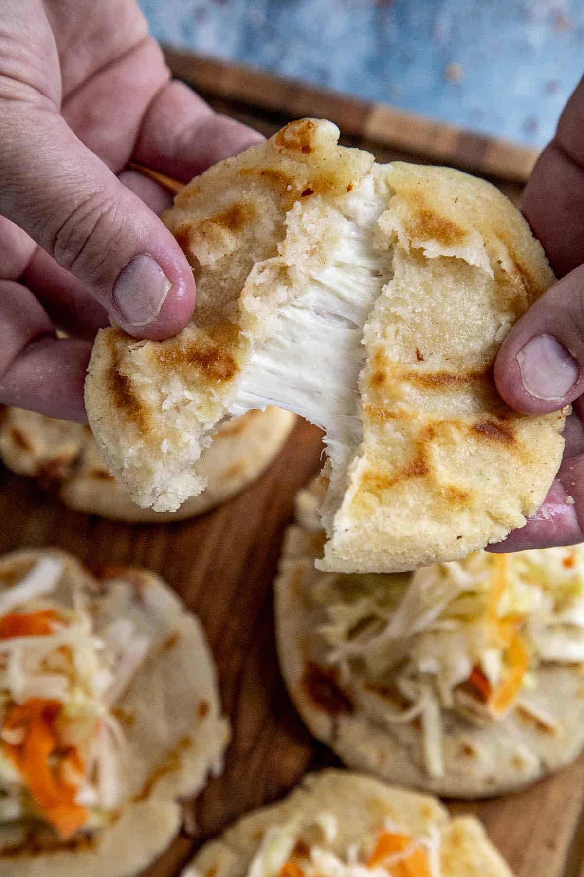 Gooey cheese stretching out from pulling apart a pupusa