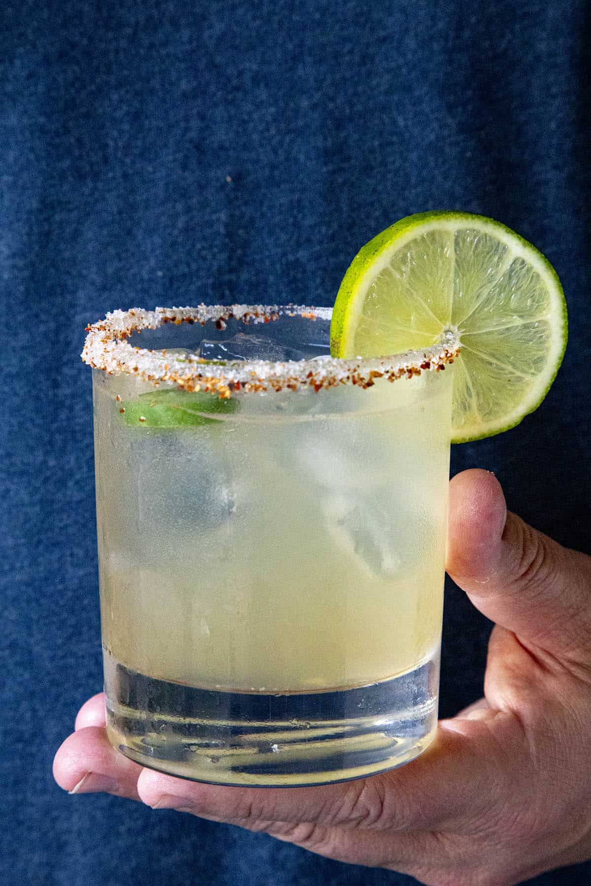 Mike holding a spicy margarita in a glass with a salt and tajin coated rim, garnished with lime and jalapeno slices