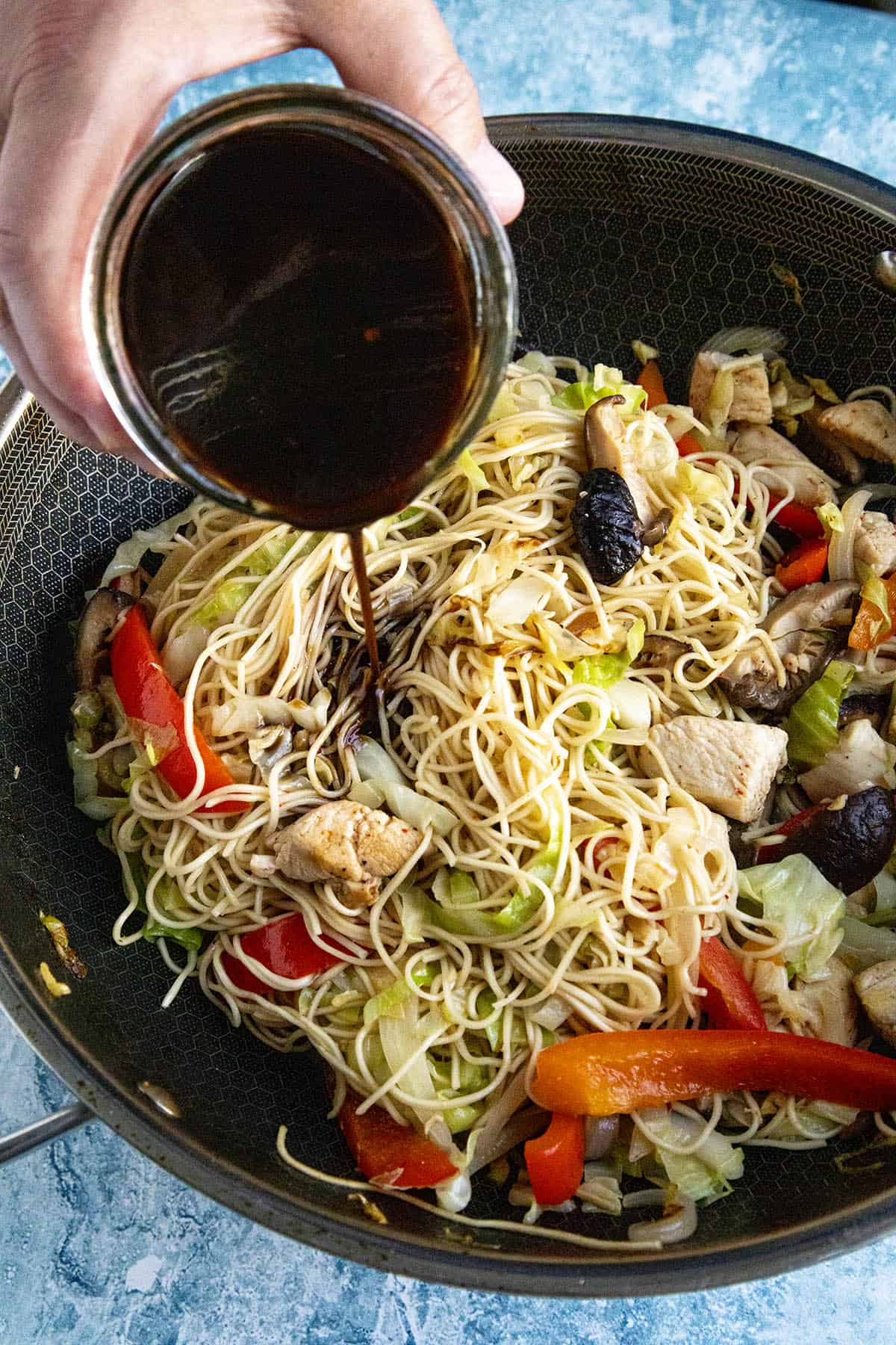 Mike pouring Yakisoba Sauce over yakisoba noodles in a pan