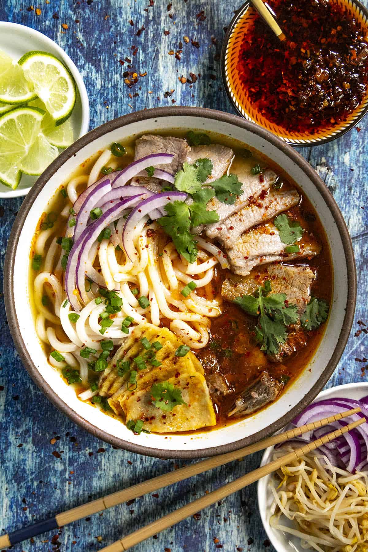 A bowl of Bun Bo Hue (Spicy Vietnamese Noodle Soup) with lots of garnish options