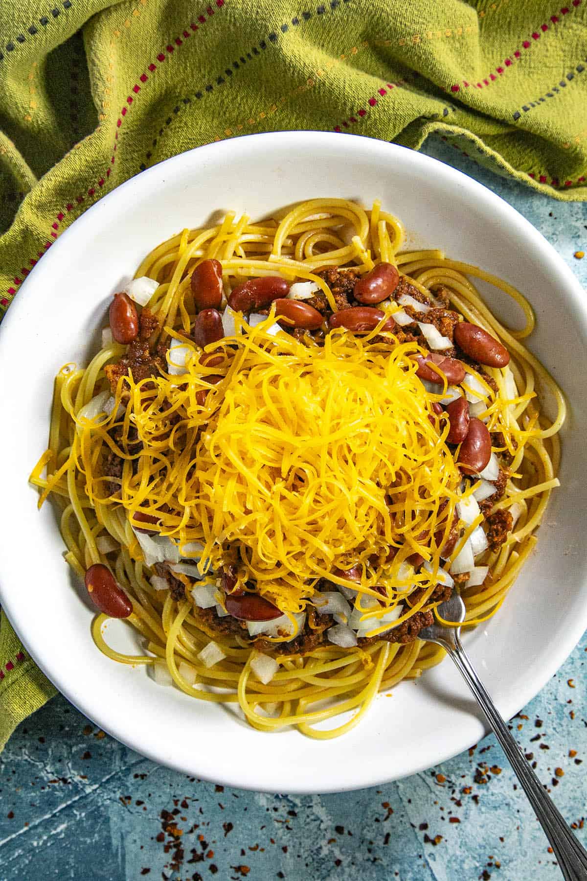 Cincinnati Chili in a bowl with spaghetti, topped with onions, beans, and cheddar cheese