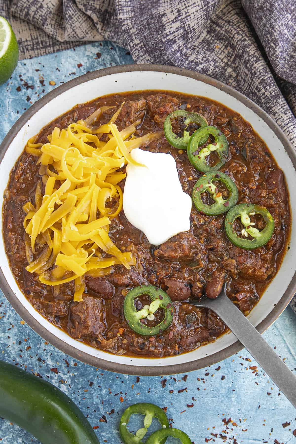 Brisket Chili in a bowl, topped with cheddar cheese, sour cream, and jalapeno slices