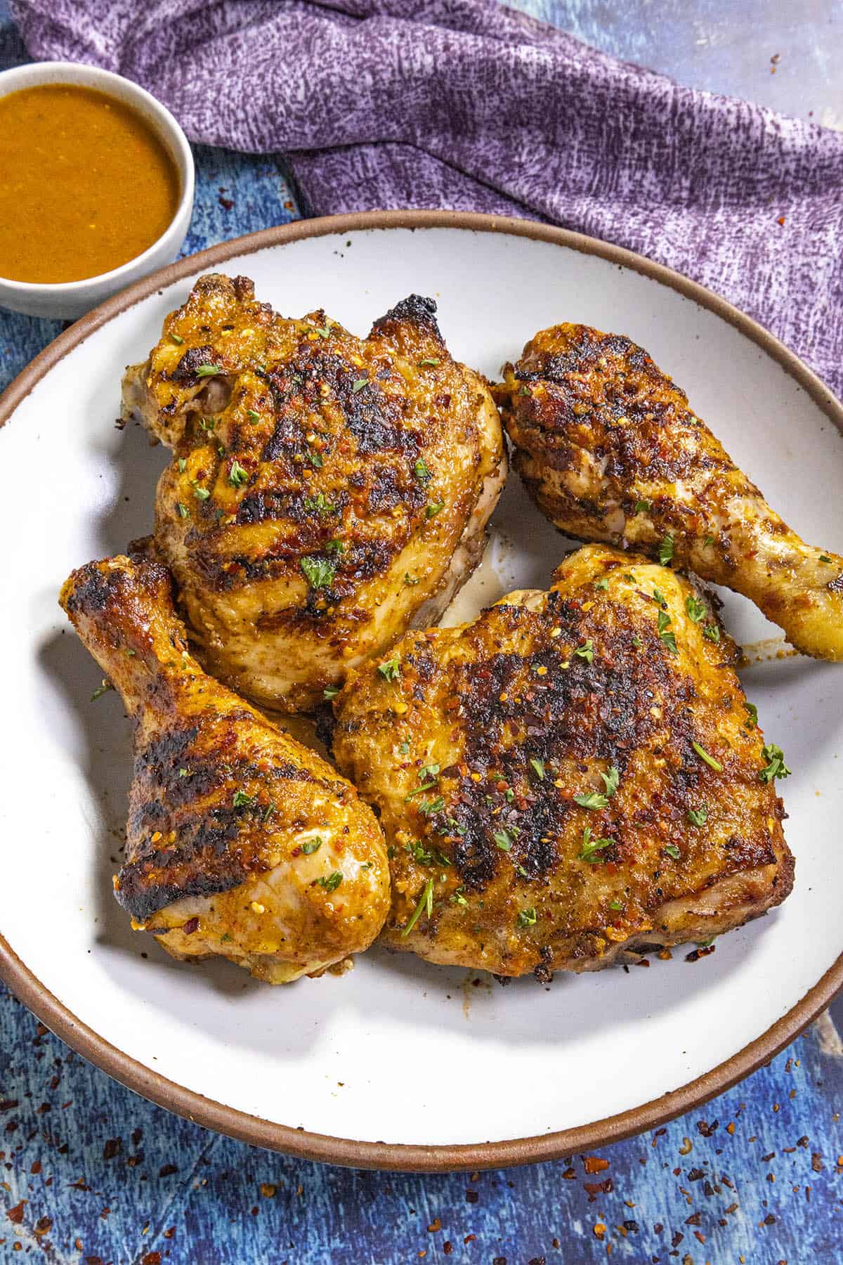Four pieces of Peri Peri Chicken on a plate, ready to serve with extra peri peri sauce on the side